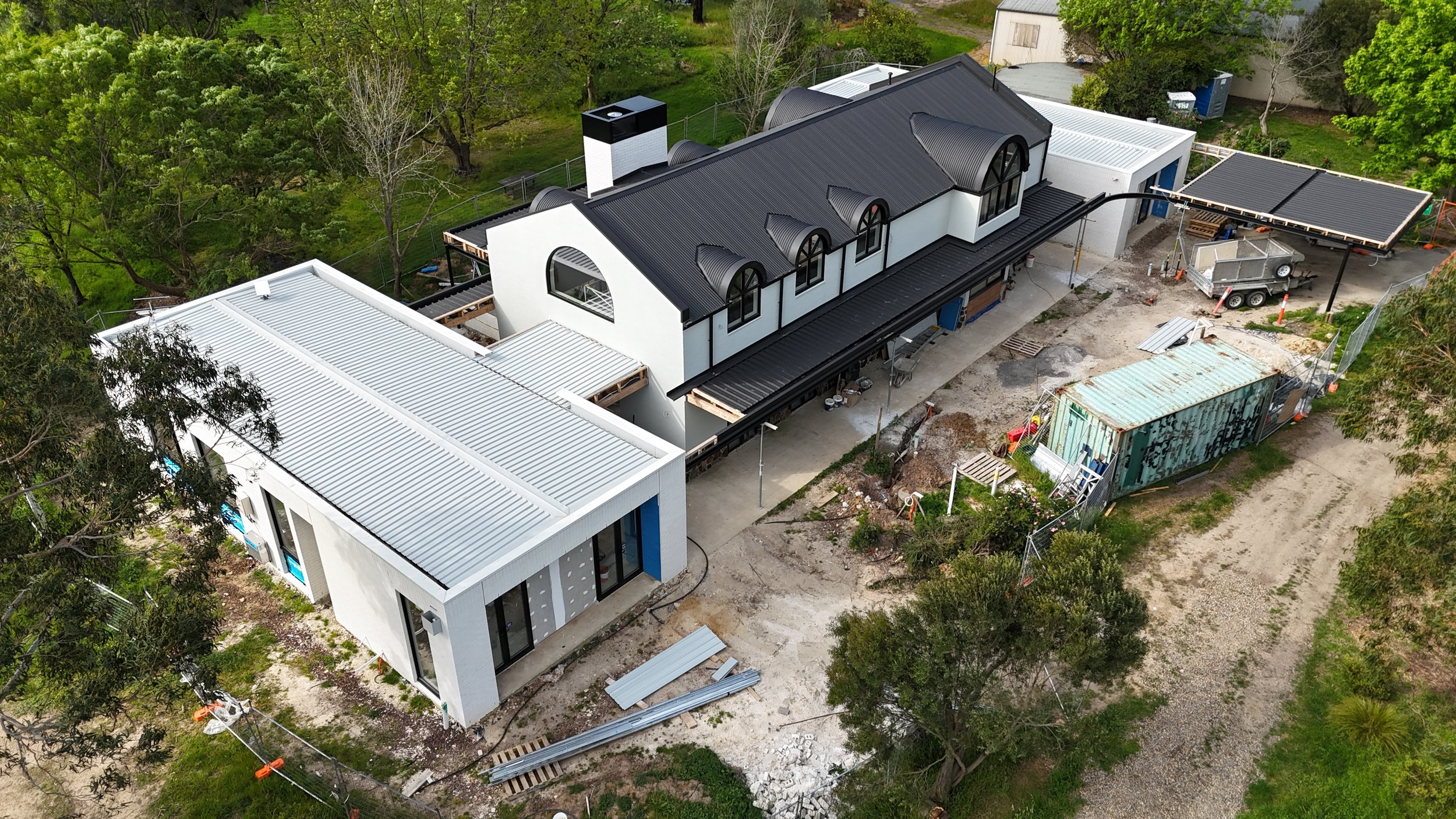 Exterior view of a building with vertical wooden slats and glass doors, reflecting the sky and trees.
