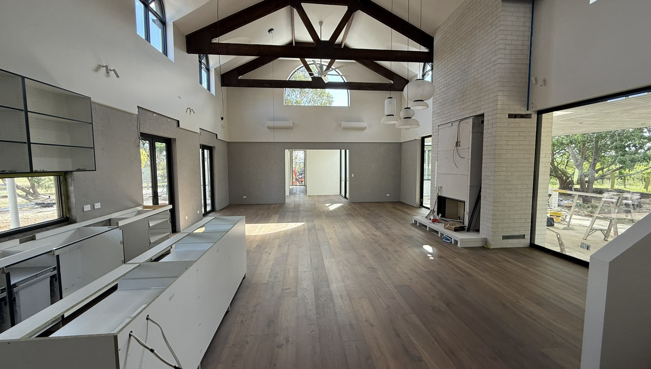 Interior of a spacious room under construction with wooden ceiling beams, large windows, and a fireplace.