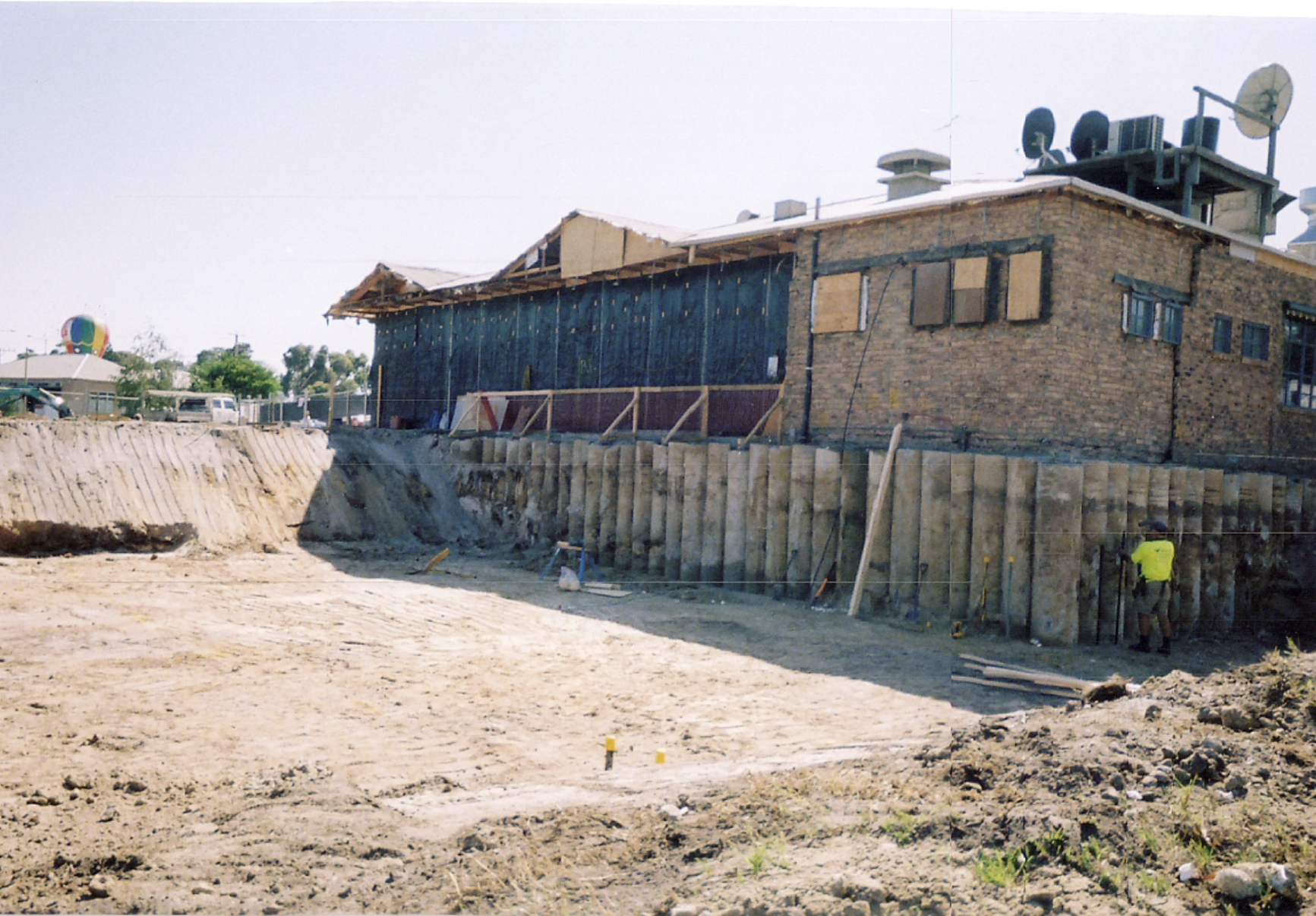 Construction site with a partially built brick and wood house, wooden support beams, and construction workers working on the foundation.