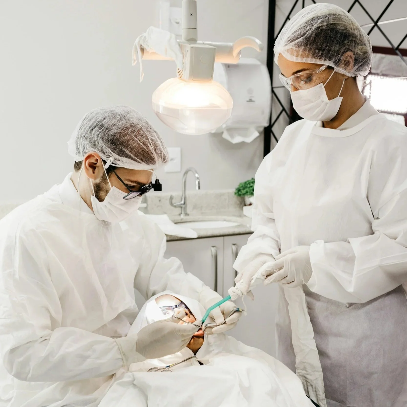 Dentists in surgical attire performing a dental procedure in a clinical setting.