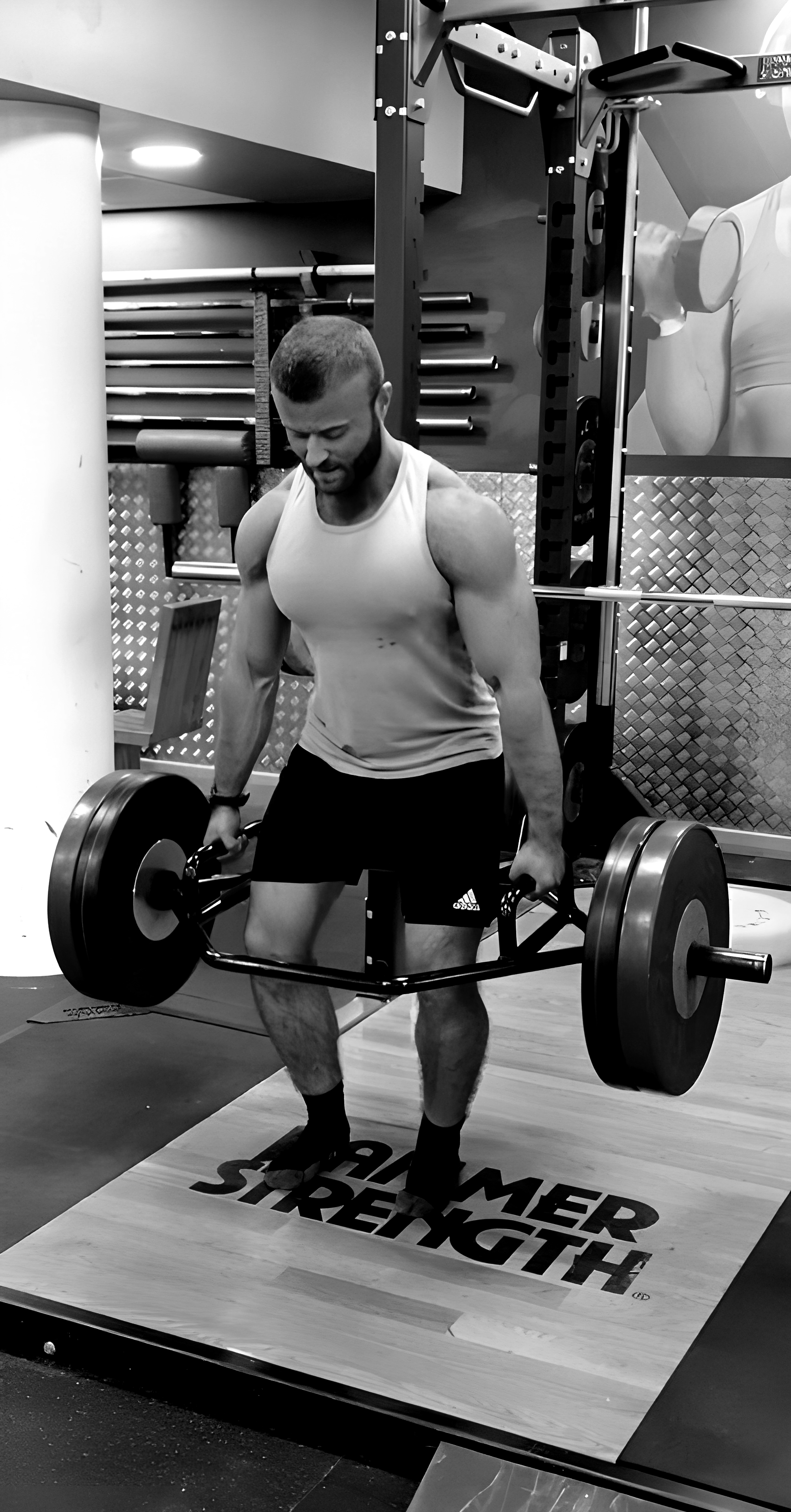 A man lifting a barbell with weights at the gym, standing on a mat that says 'HARPER STRENGTH'.