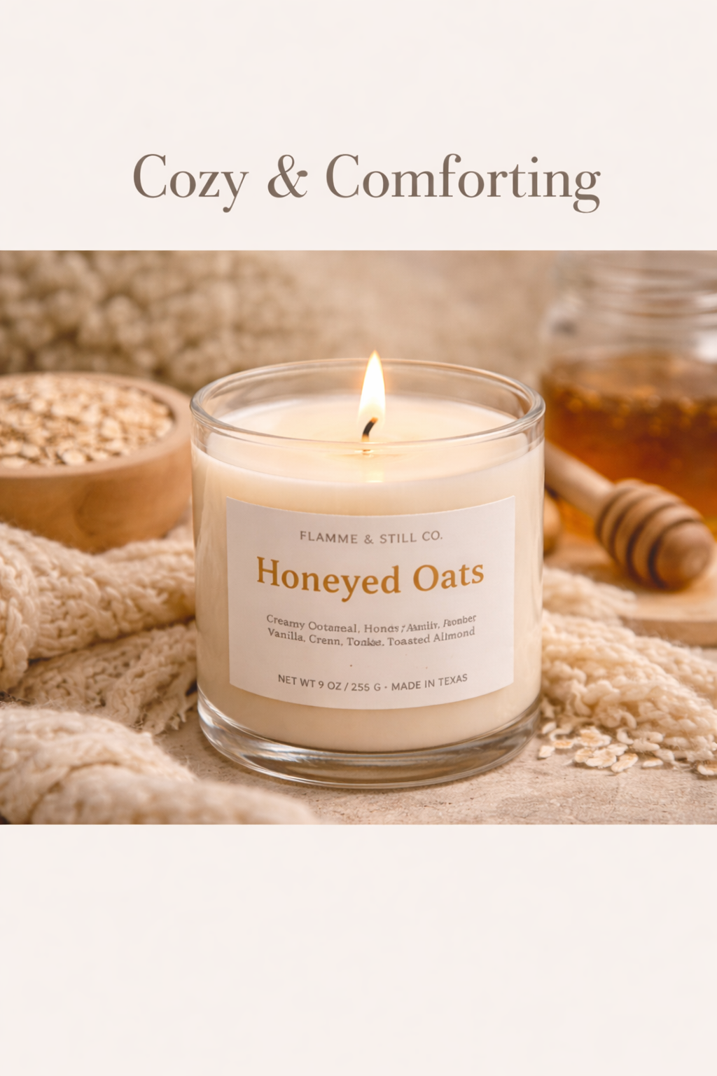 A candle labeled Honeyed Oats from Flamme & Still Co. with a lit wick, surrounded by oatmeal, honey, and a honey dipper on a cozy textured fabric.