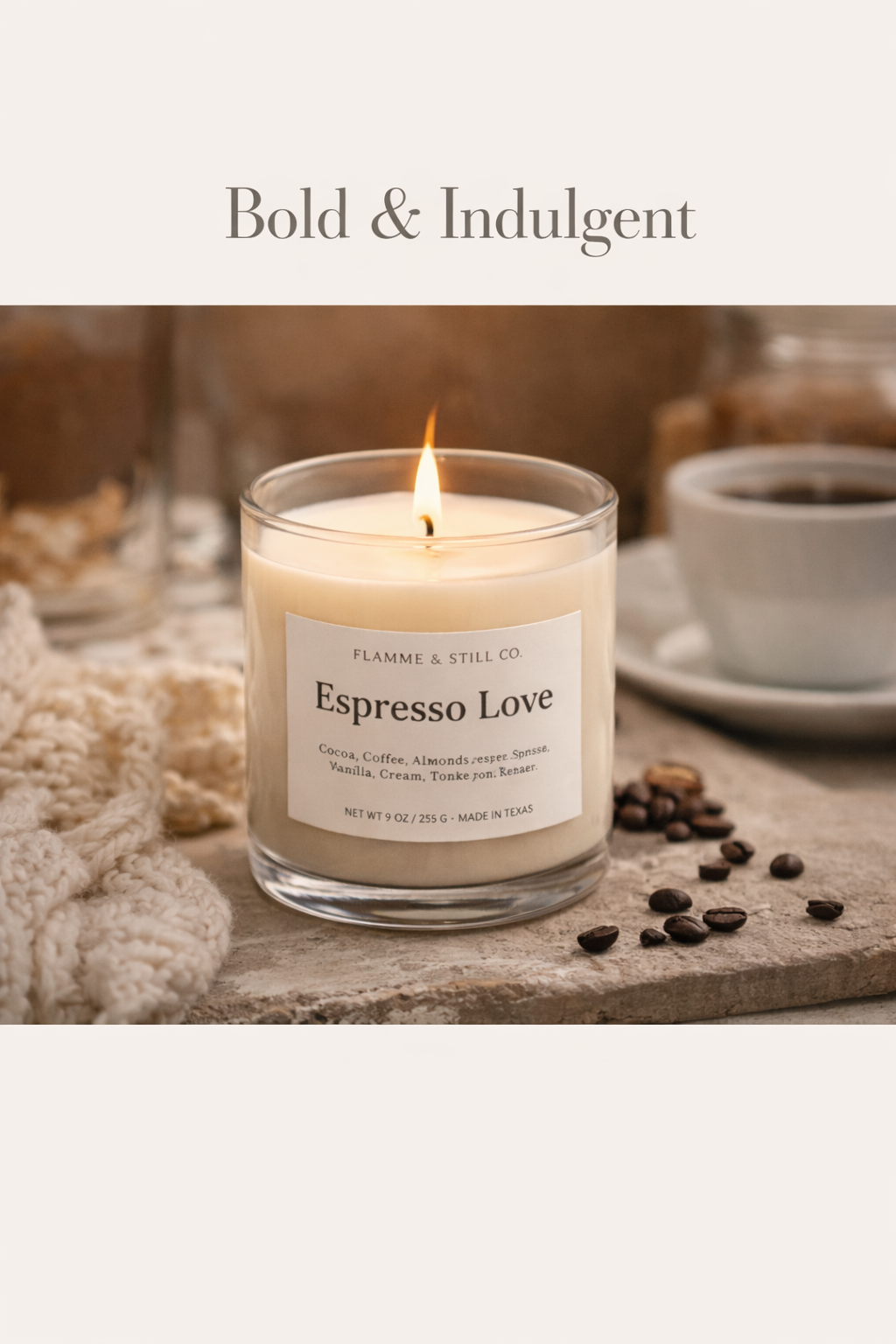 A lit scented candle labeled 'Espresso Love' from Flamme & Still Co., surrounded by coffee beans, with a cup of coffee in the background, set on a rustic surface.