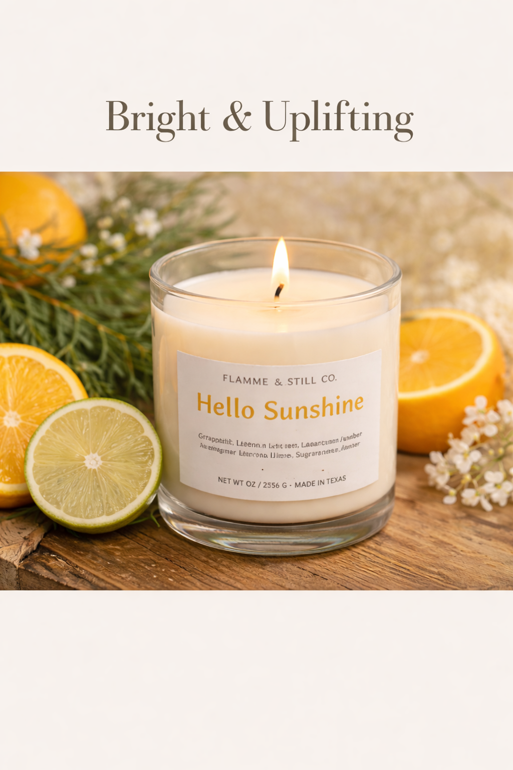 A lit scented candle labeled Hola Sunshine surrounded by halved oranges, lemons, and white flowers on a wooden surface.