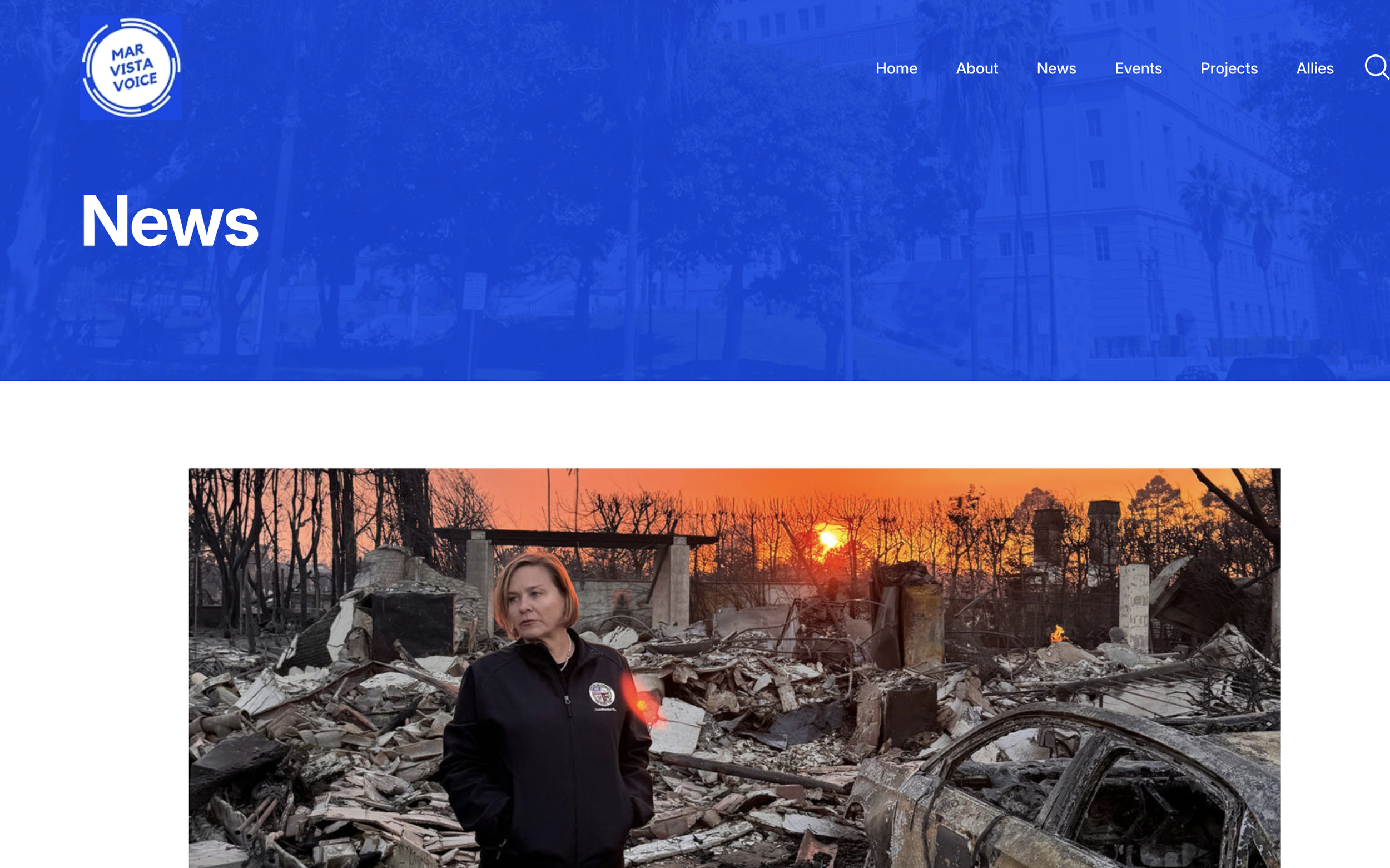 A woman standing amidst the wreckage of a fire or explosion, with destroyed cars and debris all around, during sunset.