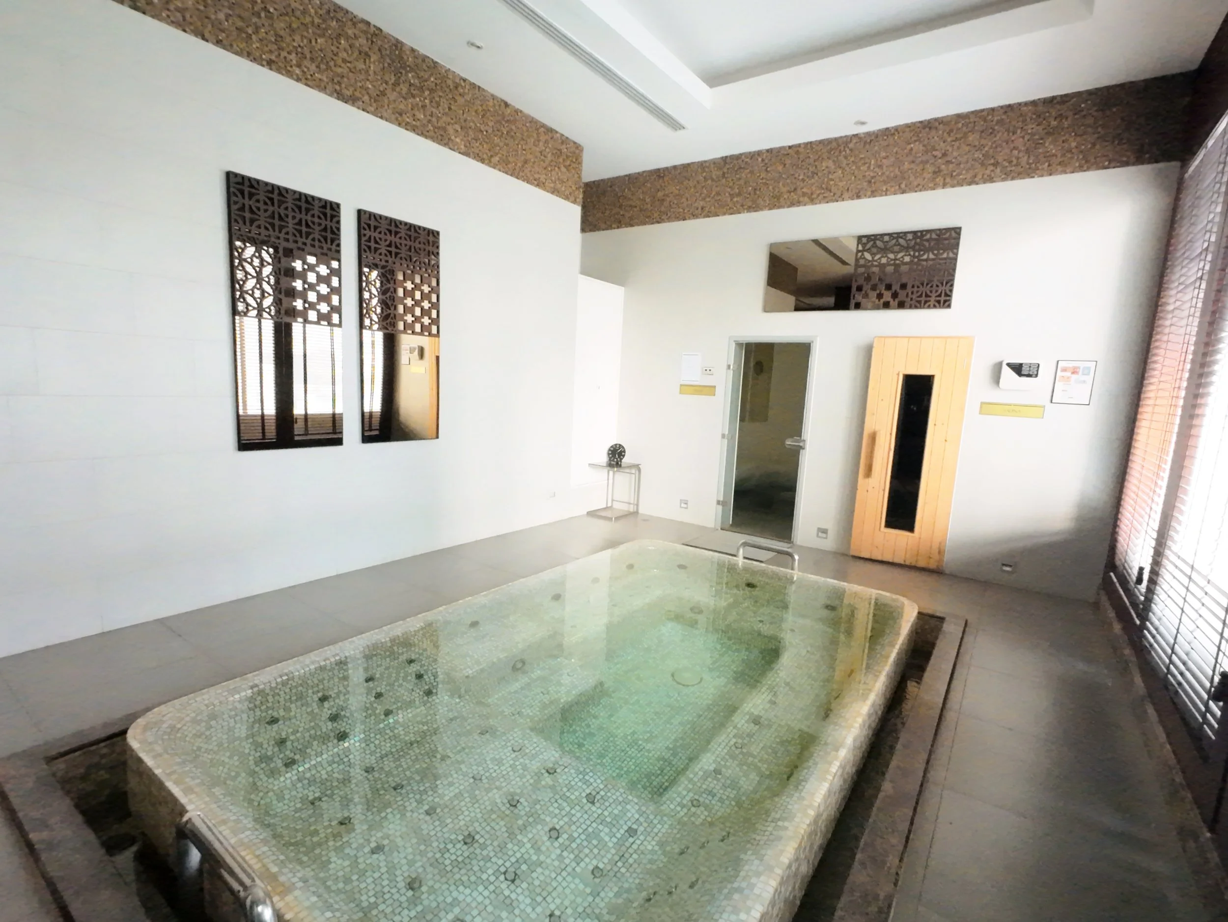 Indoor spa or pool area with a small tiled pool, wood-paneled wall feature, decorative wall panels, and windows with shutters.
