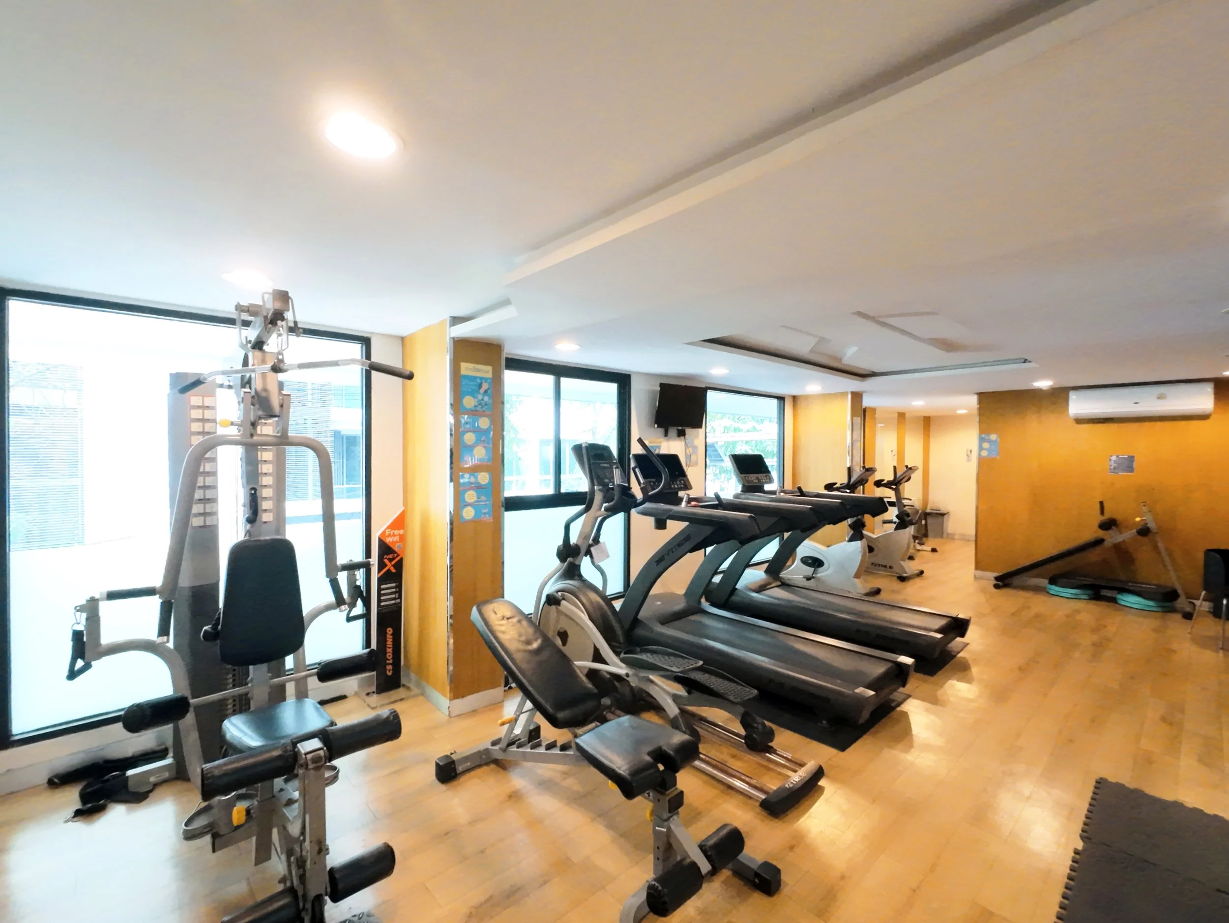 A fitness center with cardio machines like treadmills and ellipticals, large windows, and motivational posters on the walls.