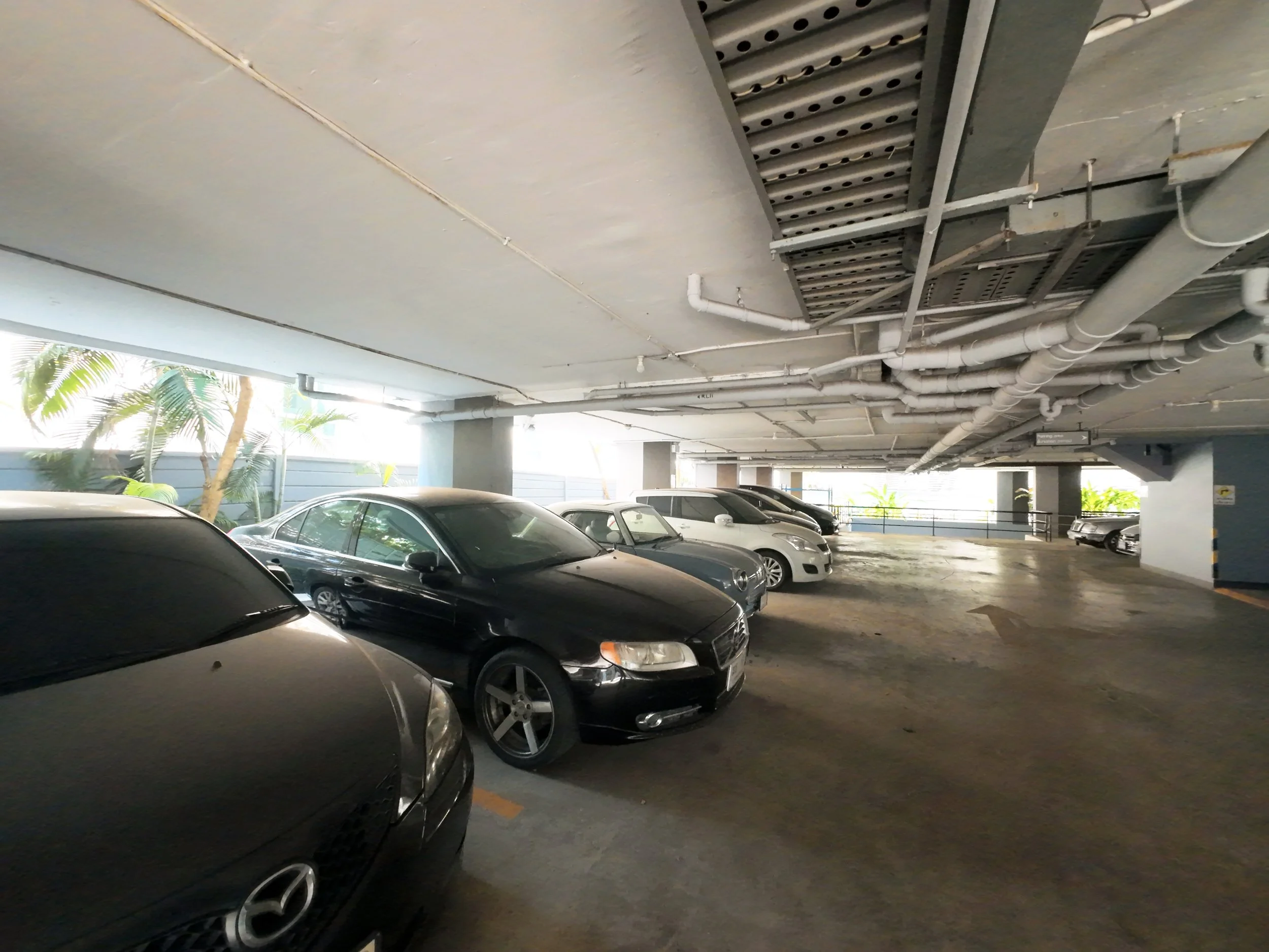 Underground parking garage with several parked cars and exposed ceiling pipes and ductwork.