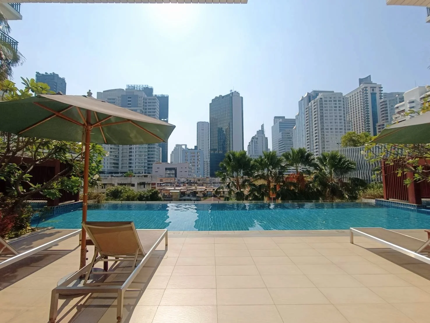 Swimming pool with lounge chairs and umbrellas overlooking a cityscape with tall buildings.