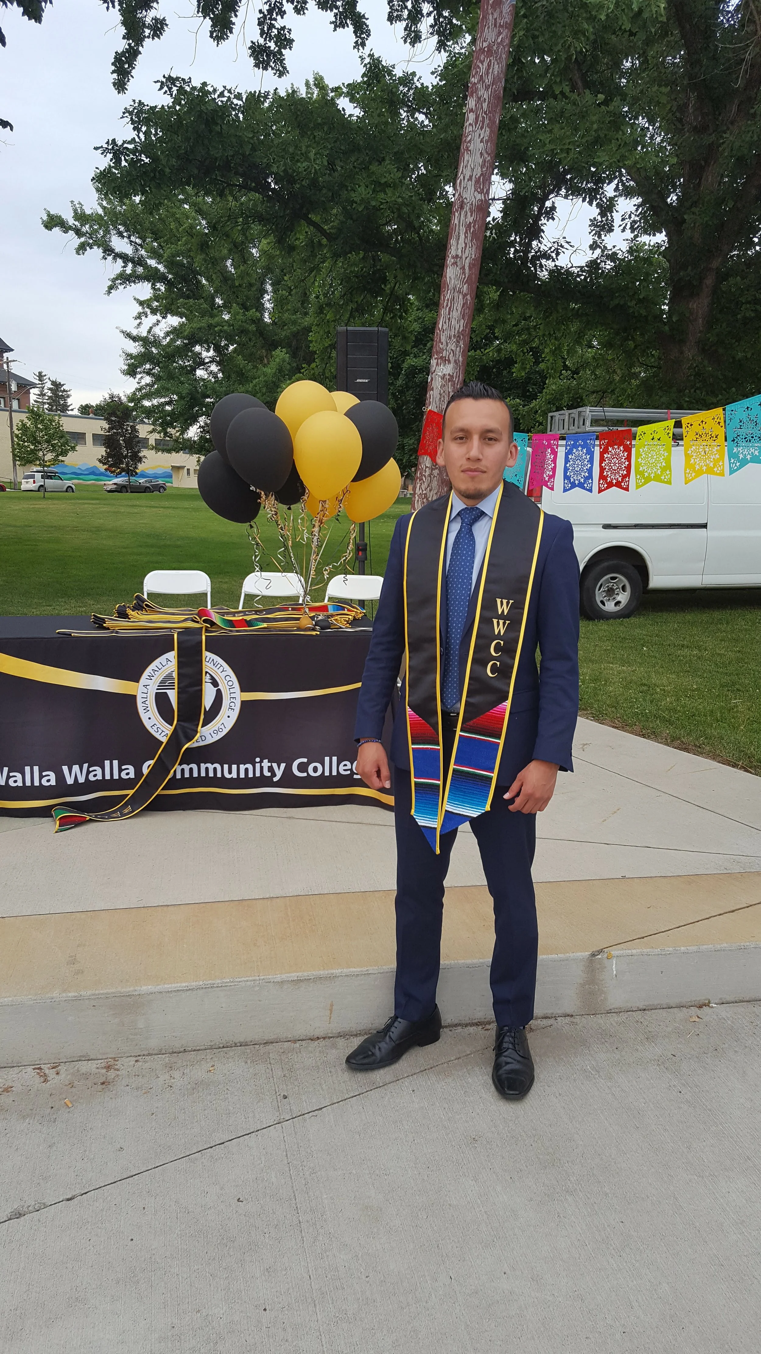 Pedro Gomez serving as keynote speaker at a Walla Walla Community College graduation, wearing a suit and WWCC stole