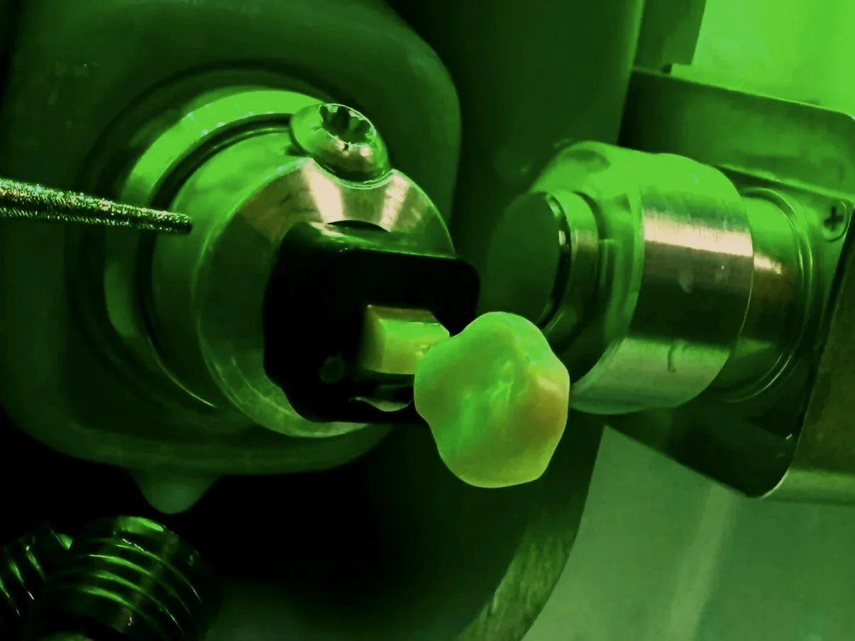 Close-up of a one-hour ceramic crown machine process. There is a drill bit working on the ceramic tooth.  illuminated with green lighting. 