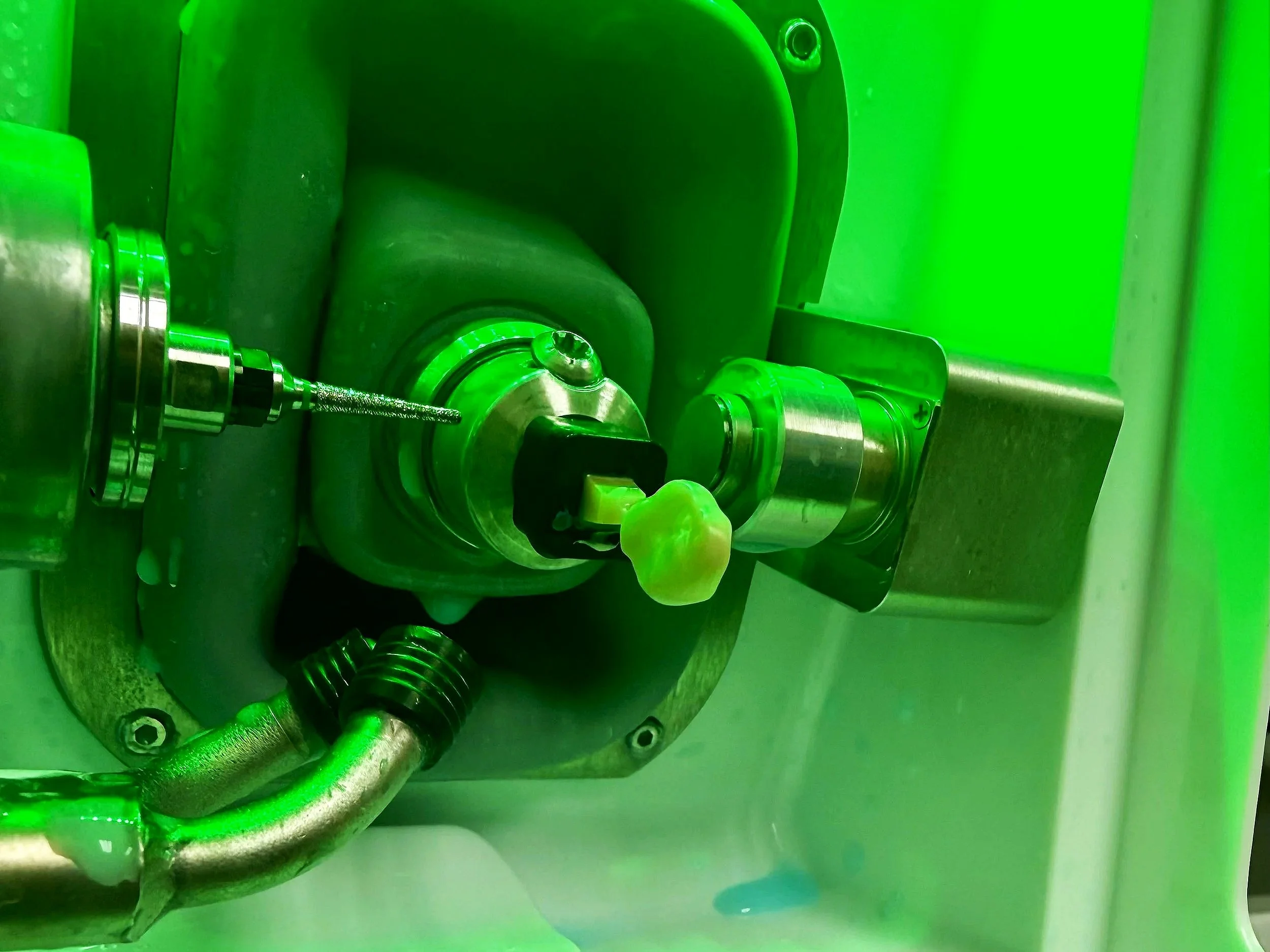 Close-up of a one-hour ceramic crown machine process. There is a drill bit working on the ceramic tooth. The whole image is illuminated by green light.