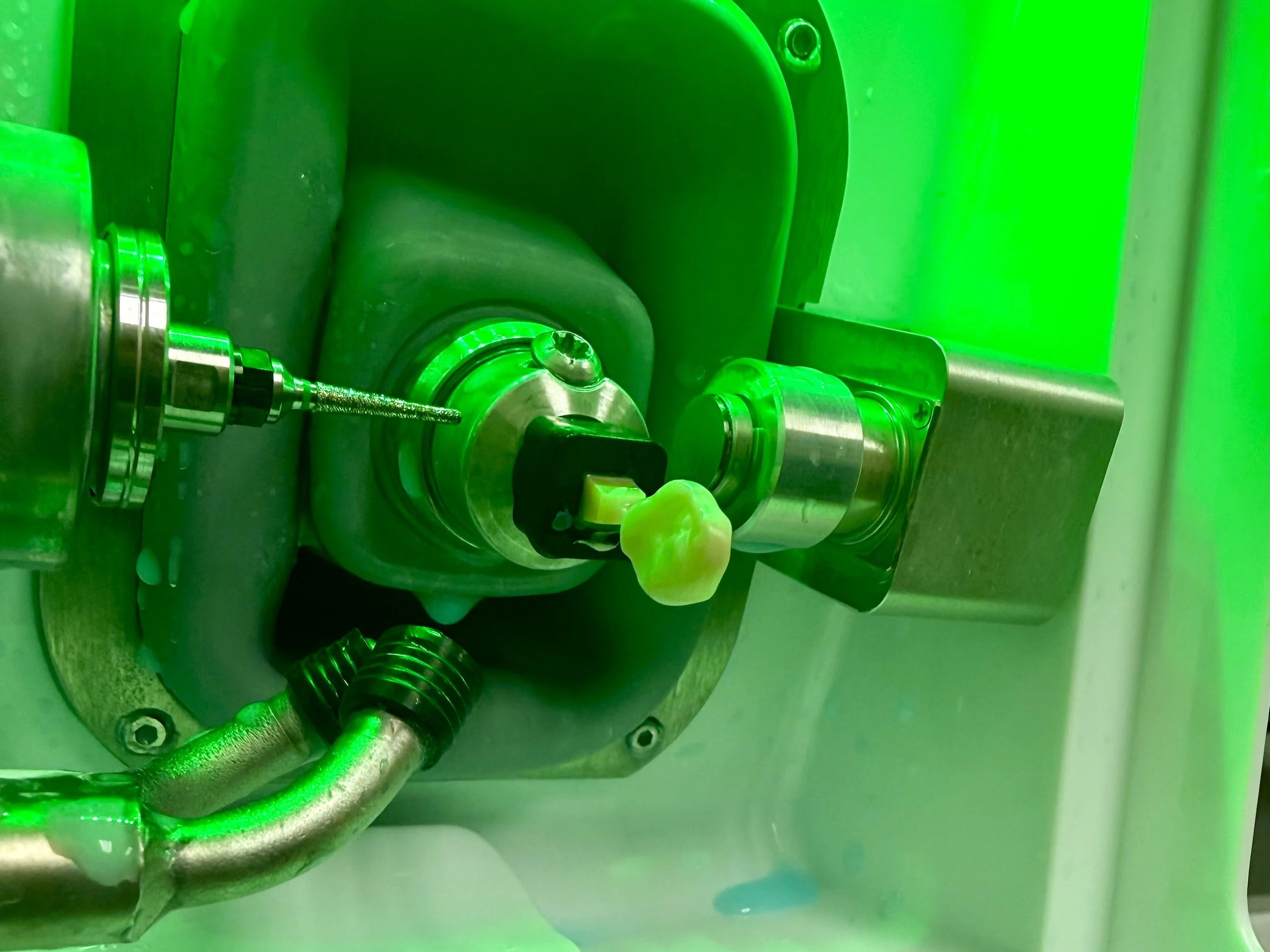 Close-up of a one-hour ceramic crown machine process. There is a drill bit working on the ceramic tooth.  illuminated with green lighting. 