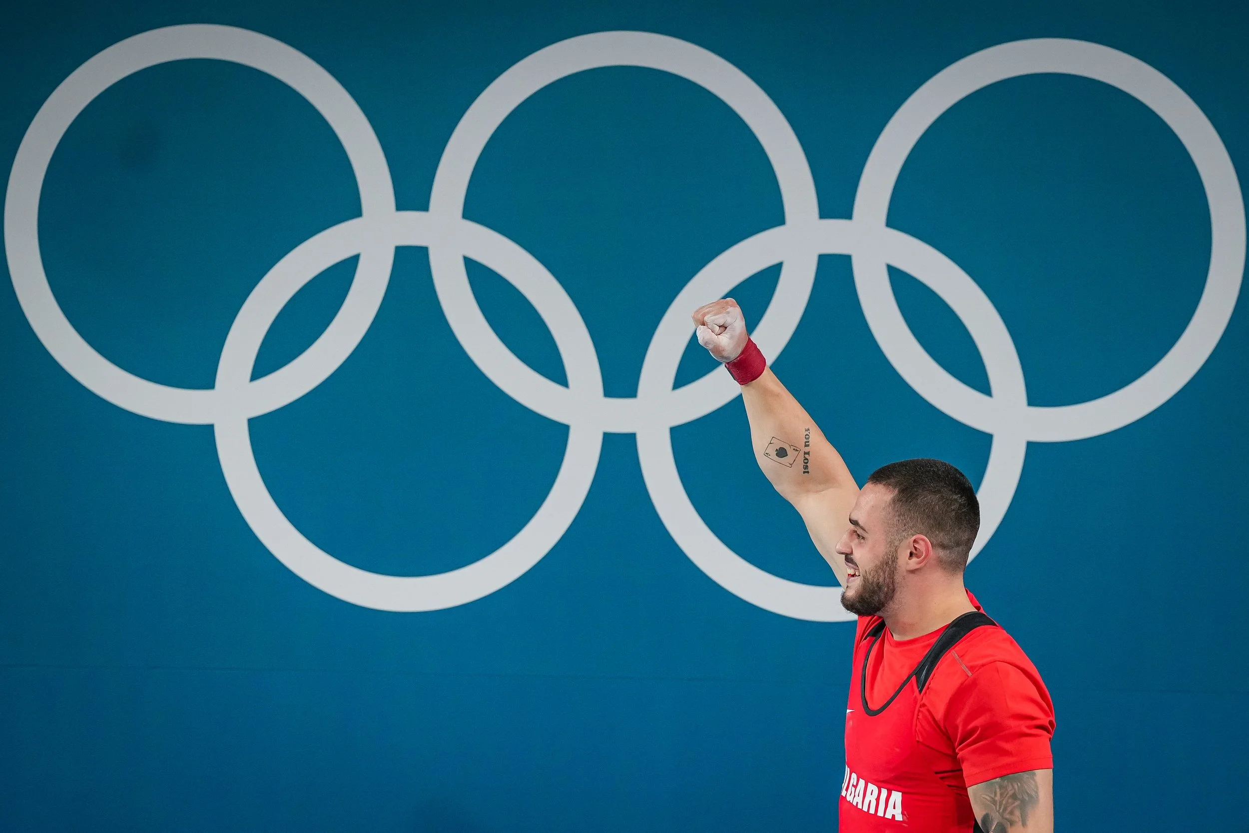 Athlete in red shirt raising his fist in front of Olympic rings background