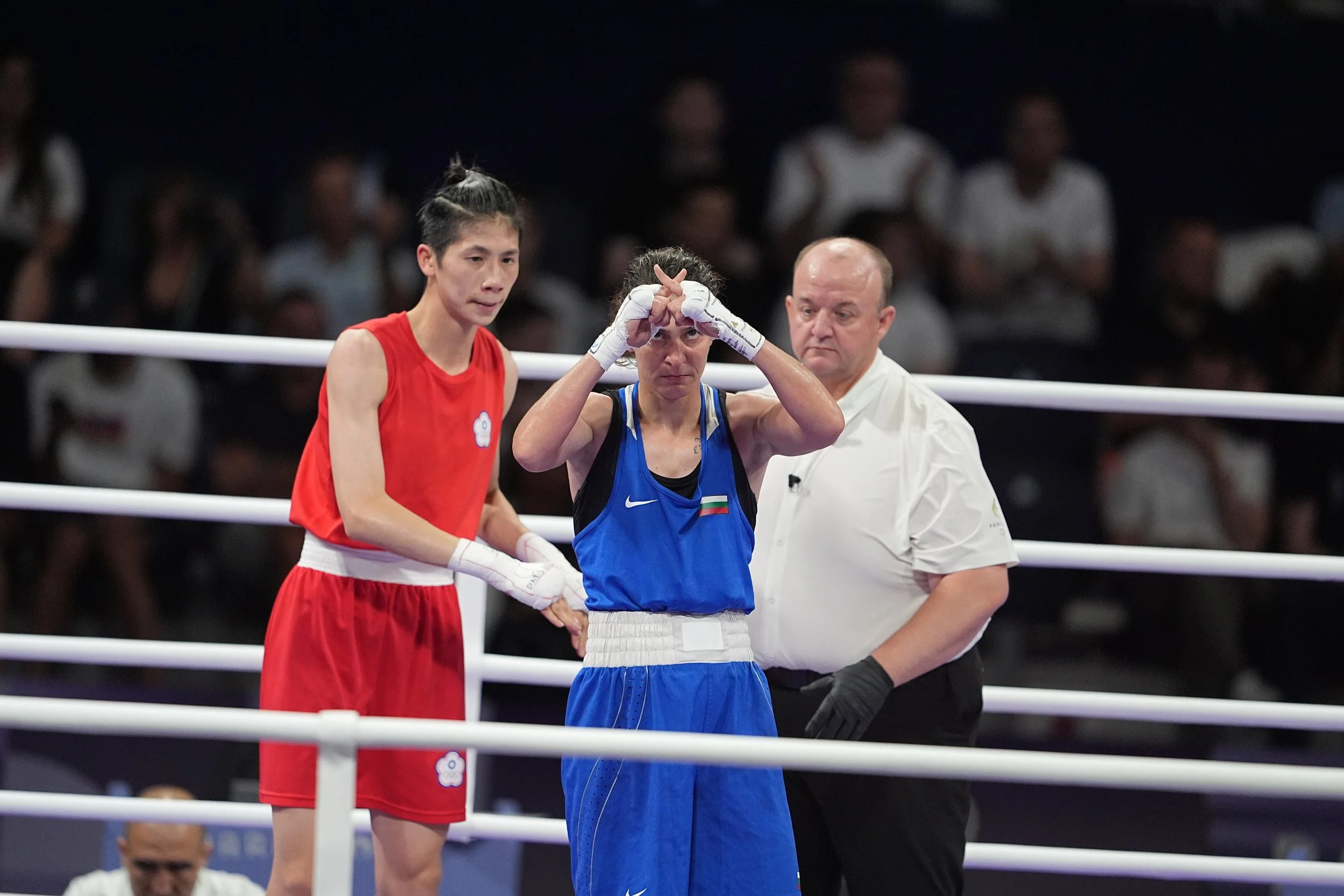 Two female boxers and a referee in a boxing ring, with one woman wearing a red uniform and the other in blue, during a match.