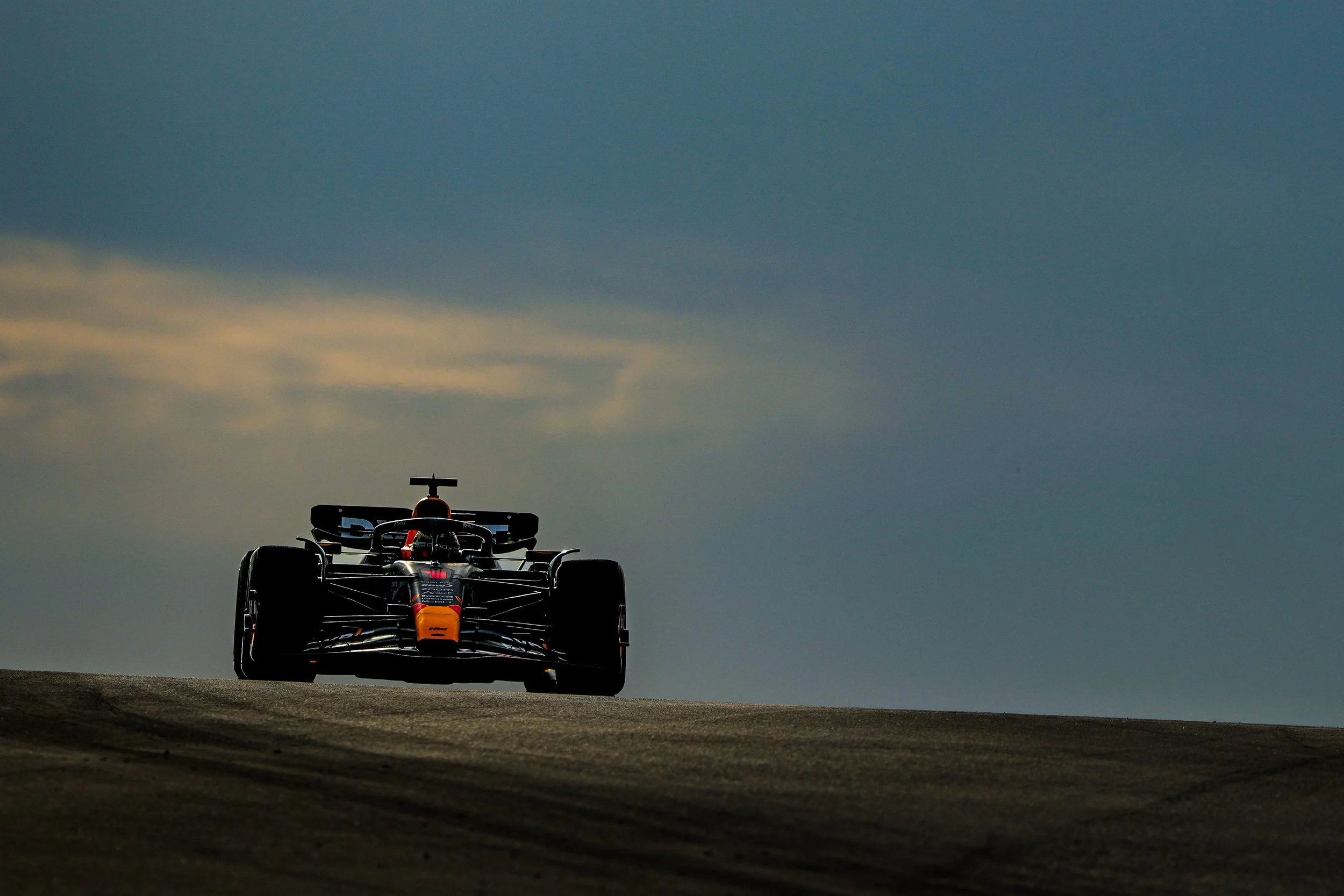 Race car driving on a track during sunset or early evening with a cloudy sky.