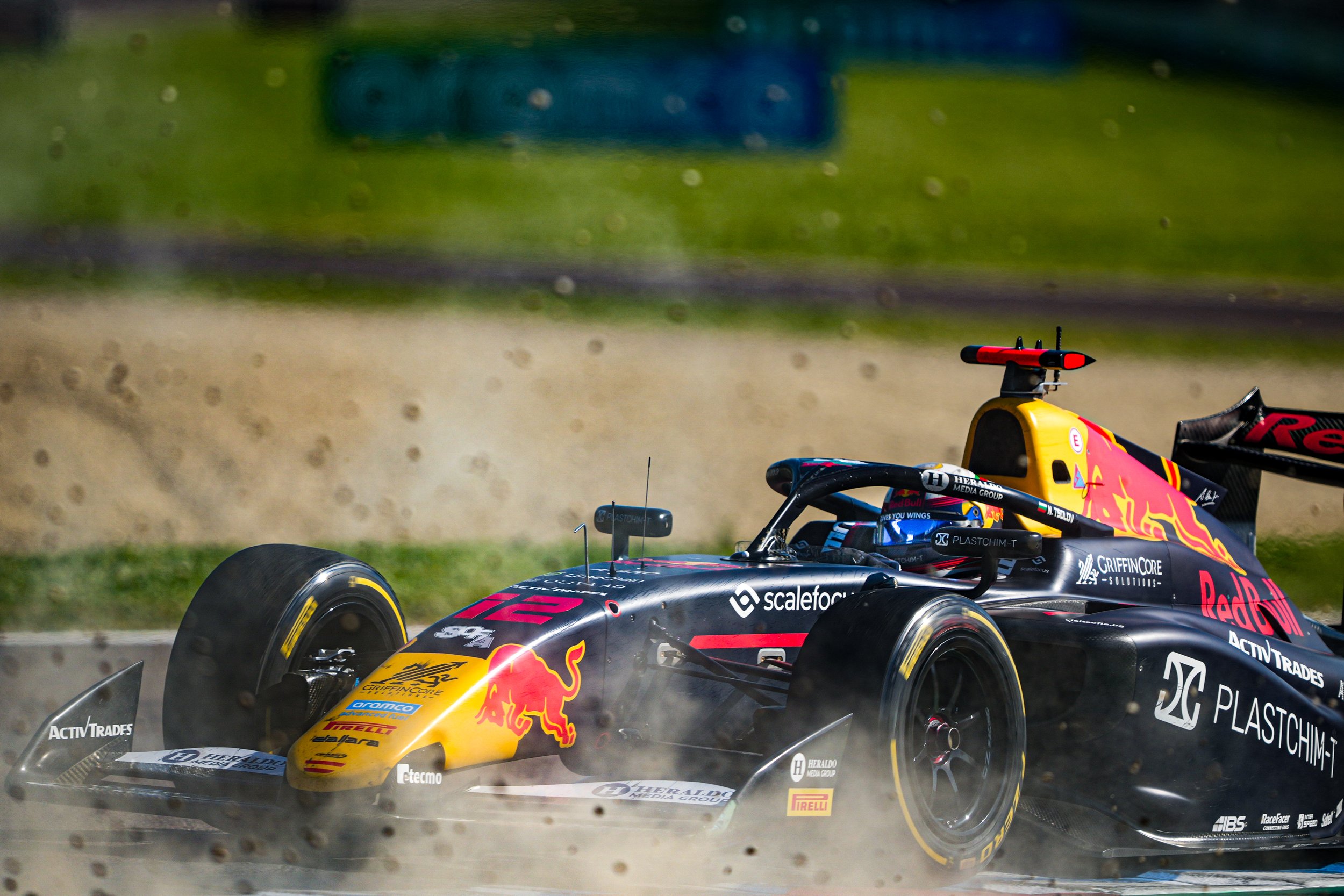 A Formula E race car kicking up dust on a racetrack with grass and barriers in the background.