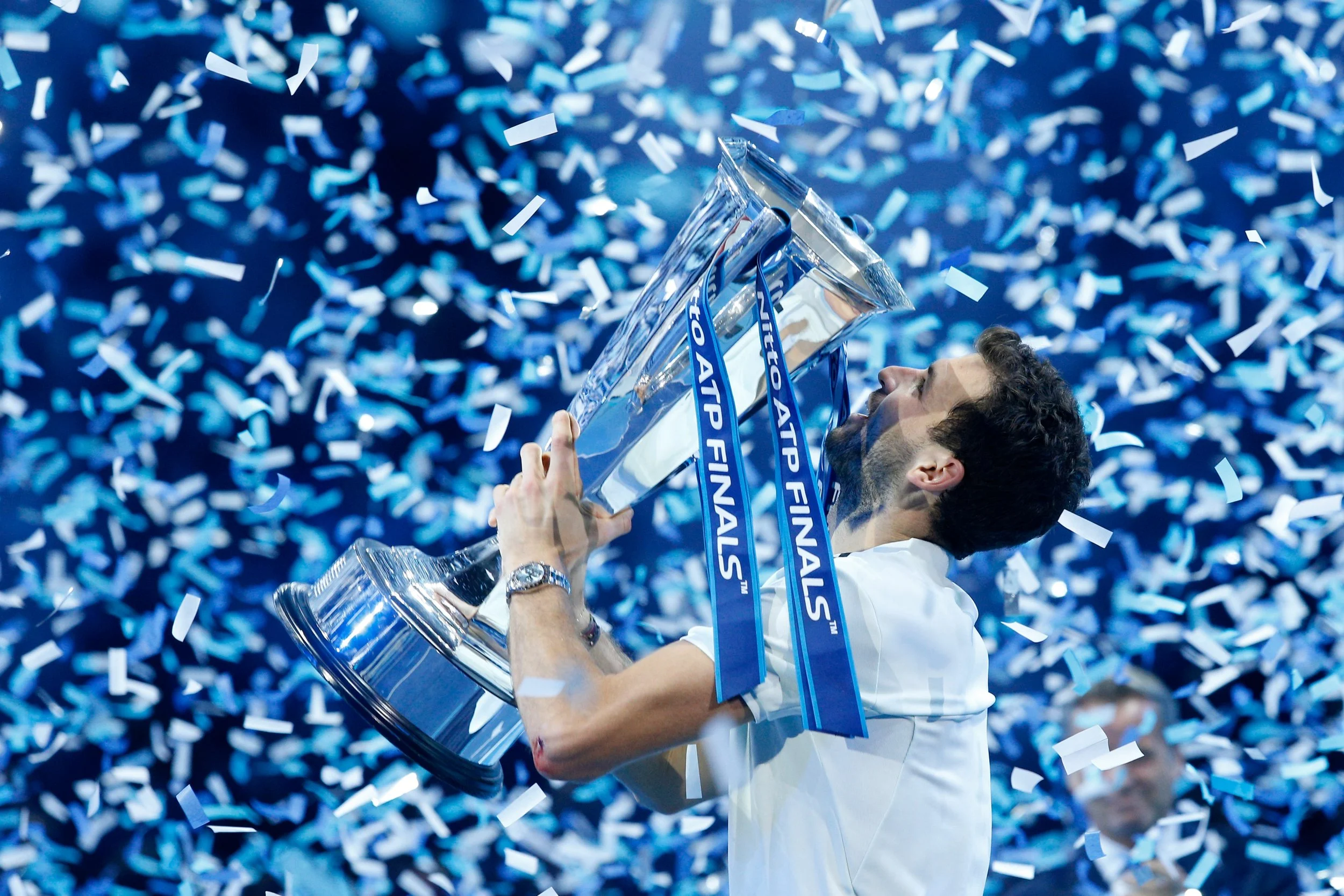 A man holding a large trophy during a celebration, with confetti falling around him, on a tennis court.