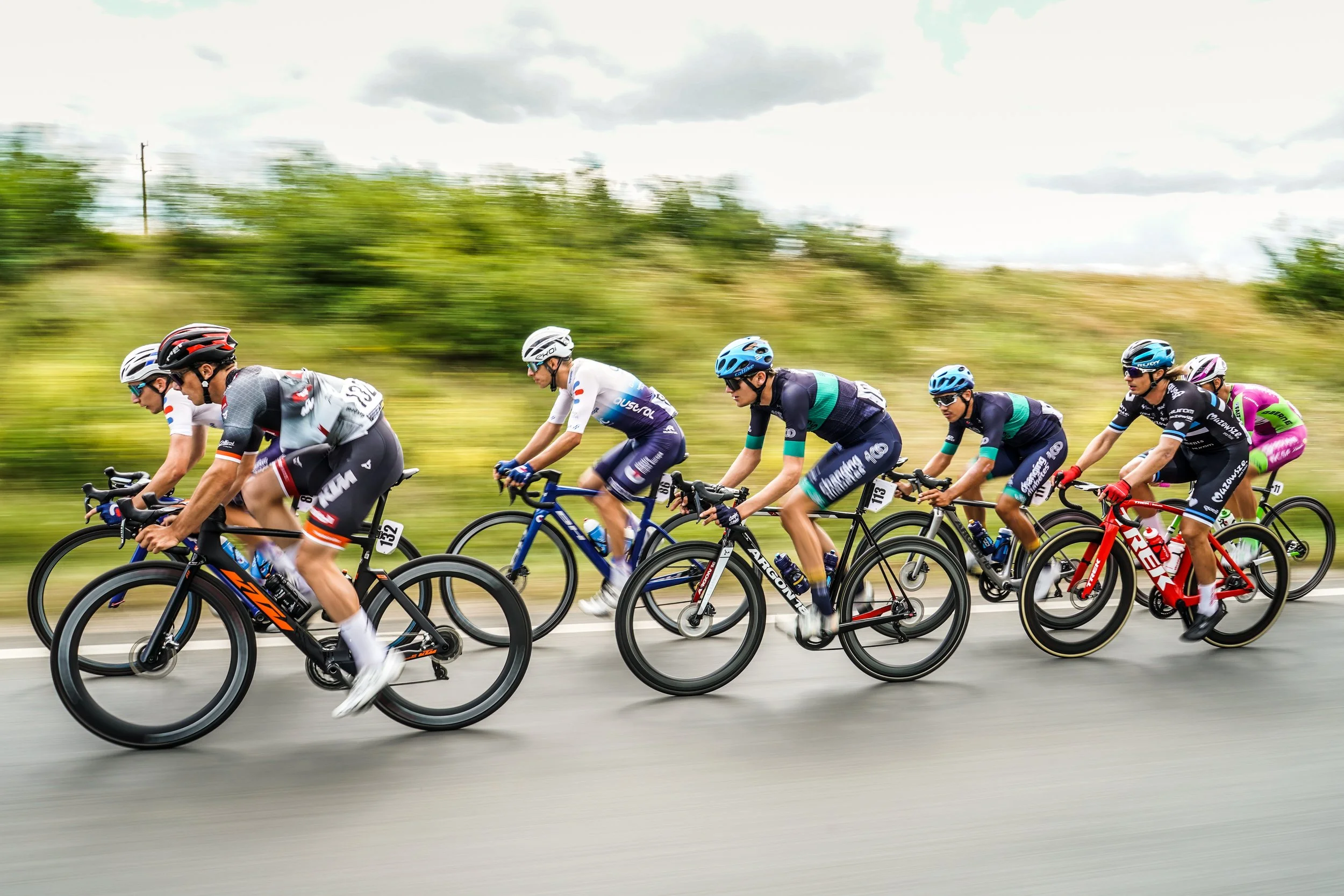 Cyclists in a race riding downhill on a paved road with green trees and cloudy sky in the background.