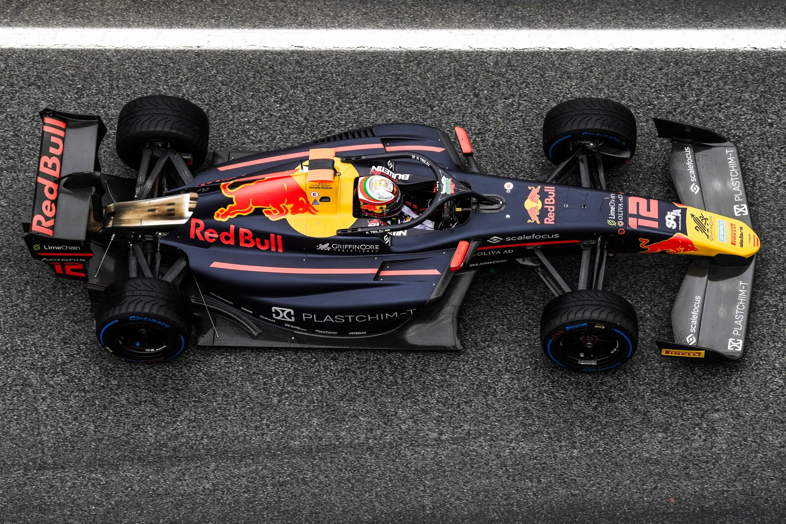 Top-down view of a black and yellow Formula racing car on a racetrack with sponsored logos, including Red Bull branding.