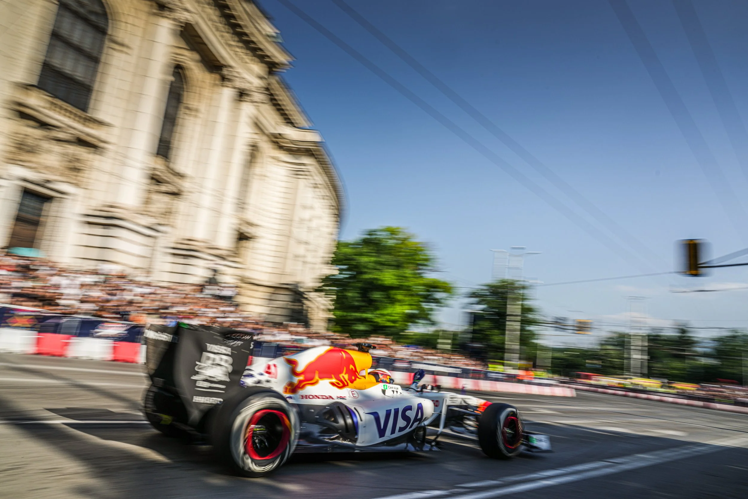 Formula 1 race car speeding through city street with blurred background, likely during a race.