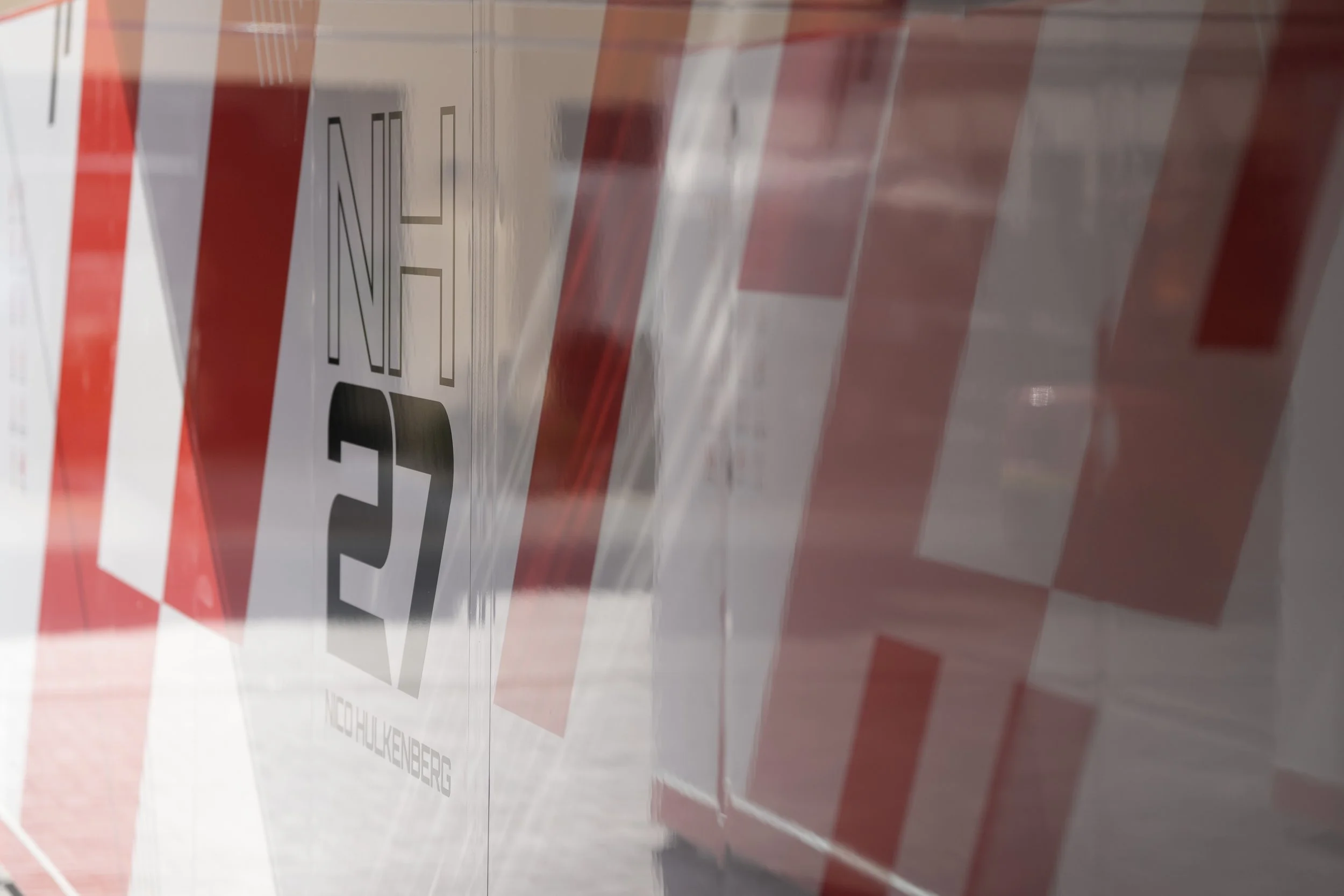 Close-up of a reflective, striped plastic barrier with a warning sign that says '2 MIN' and 'NO HULKENBERG' at an angle, reflecting the surroundings.