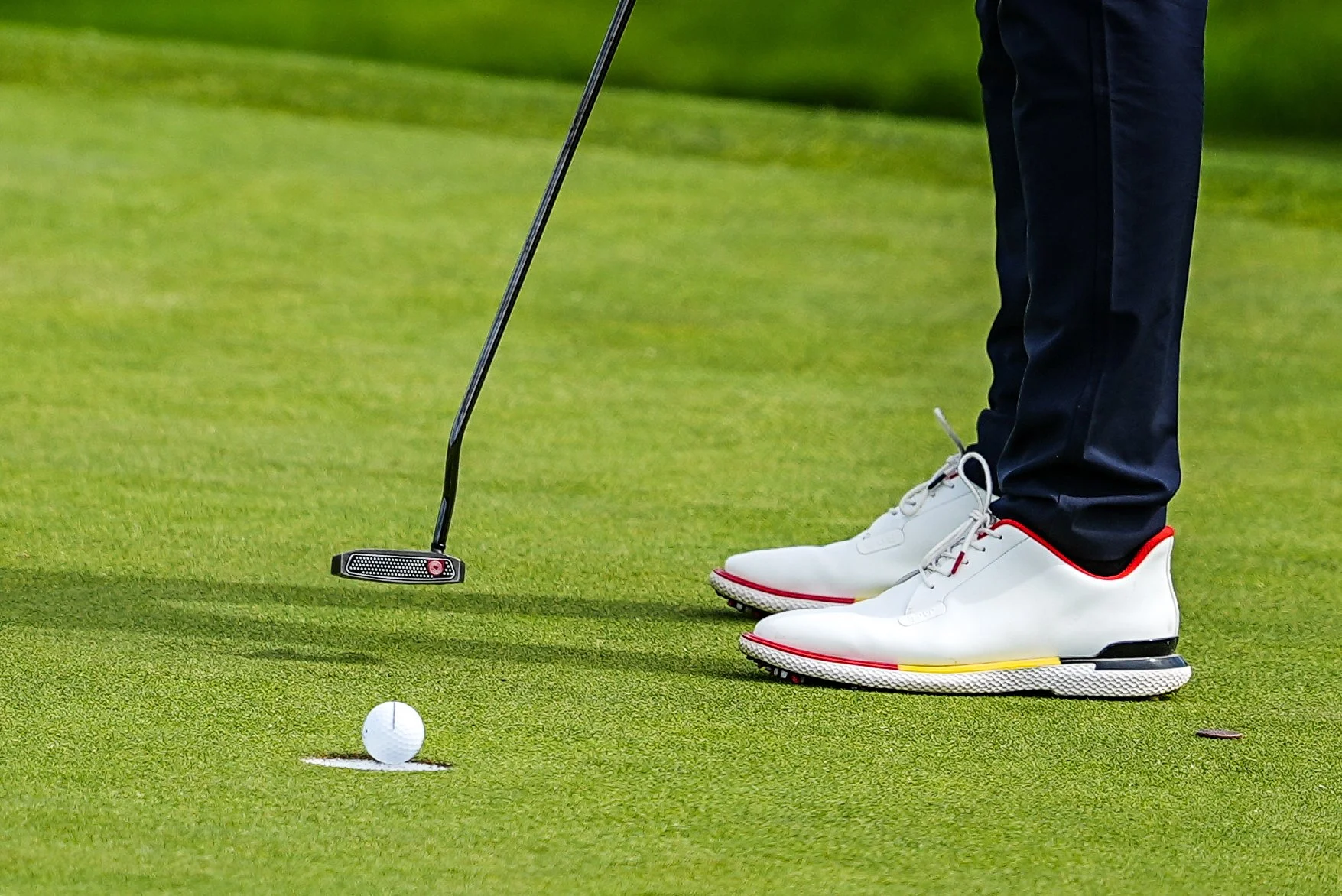 Close-up of a golfer preparing to putt the golf ball on the green, with focus on their white golf shoes and putter.
