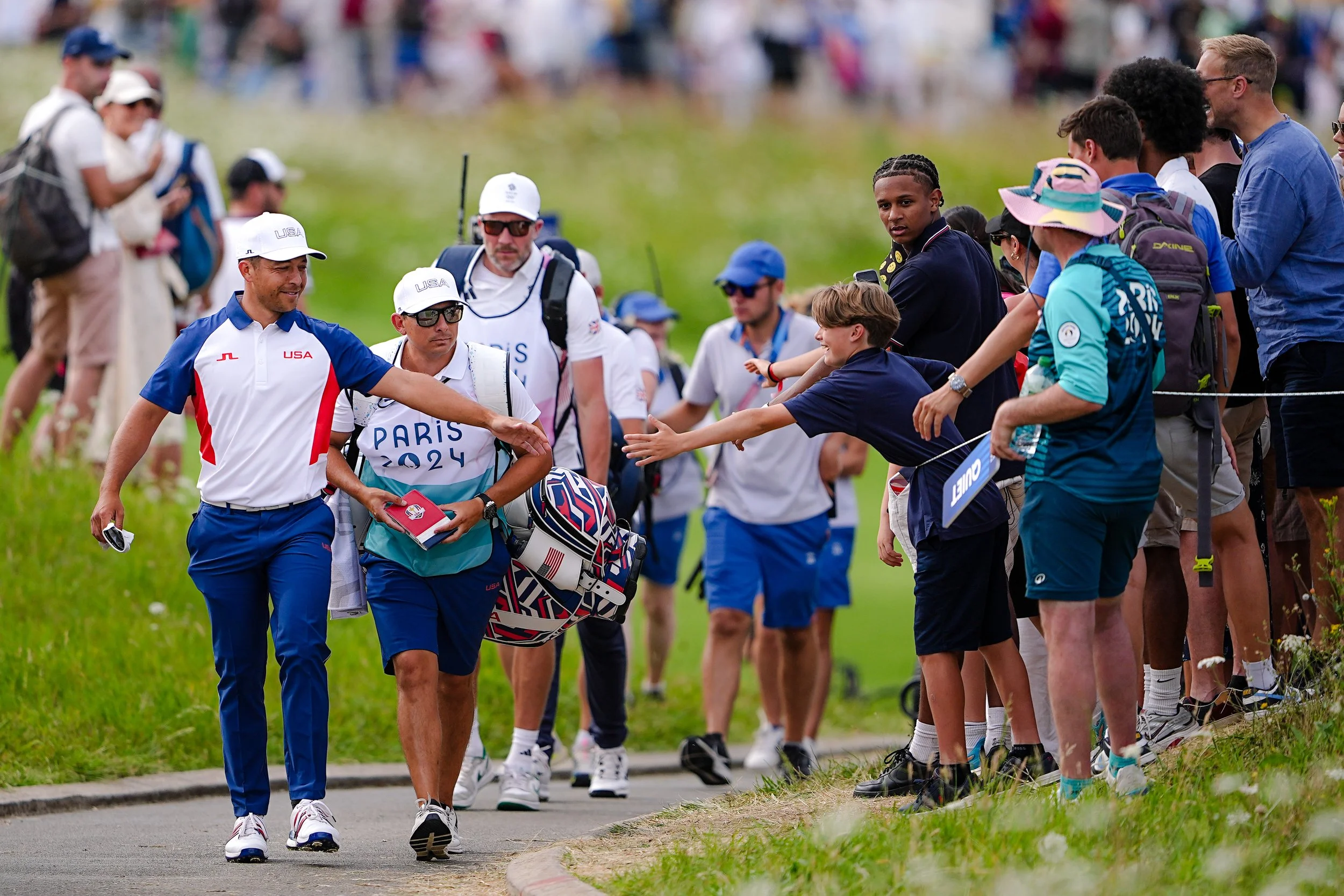 Golf players and spectators meet and shake hands on a golf course pathway during the Paris 2024 Olympics.
