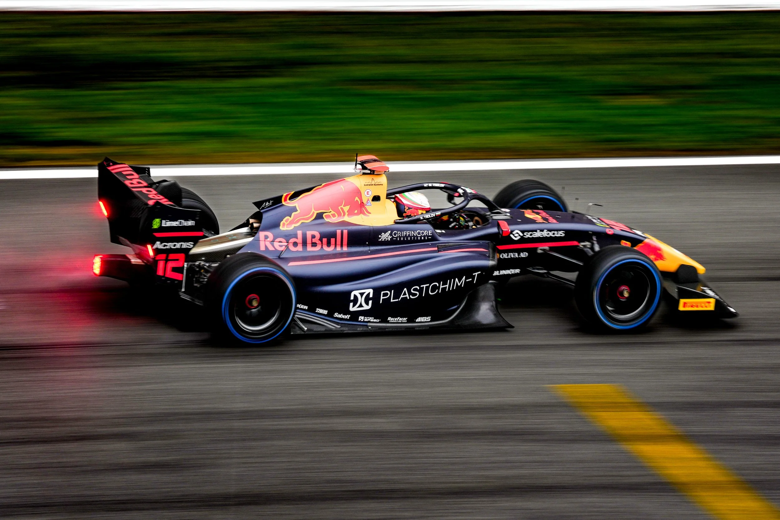 Race car speeding on a track with sponsor logos, Red Bull branding, and a yellow and black front wing.