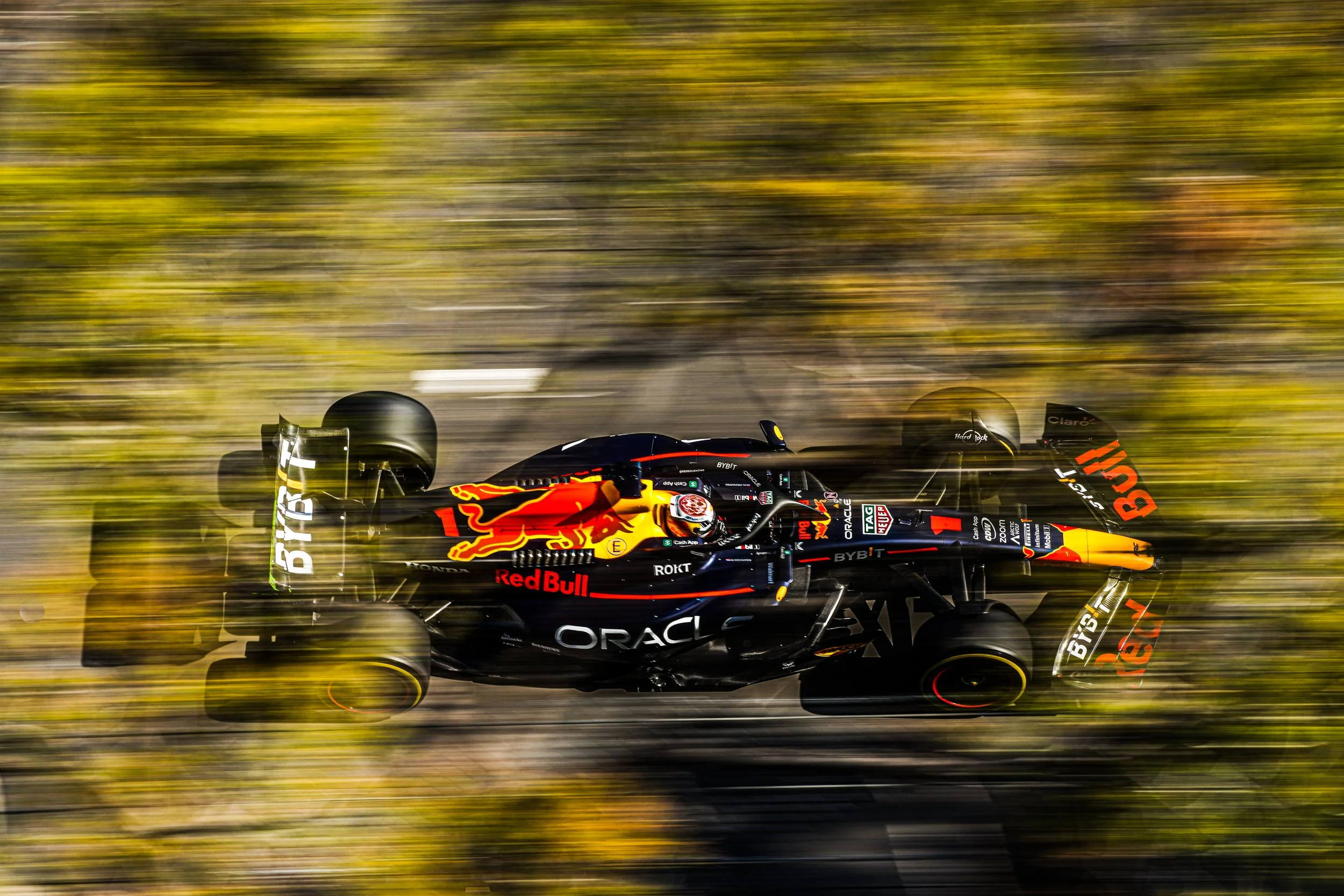 An open-wheel race car speeding on a track with a motion blur background, featuring Red Bull and Oracle logos.