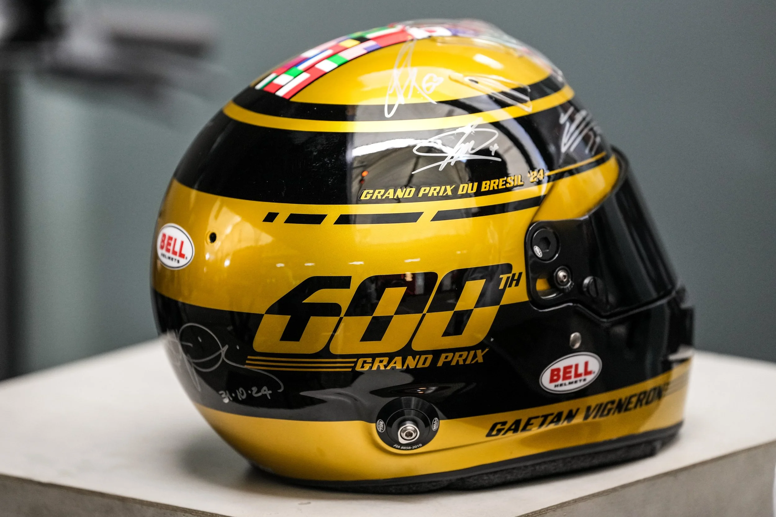Black and yellow racing helmet with signatures and sponsor logos, commemorating Gaetan Vigneron at the 60th Grand Prix.