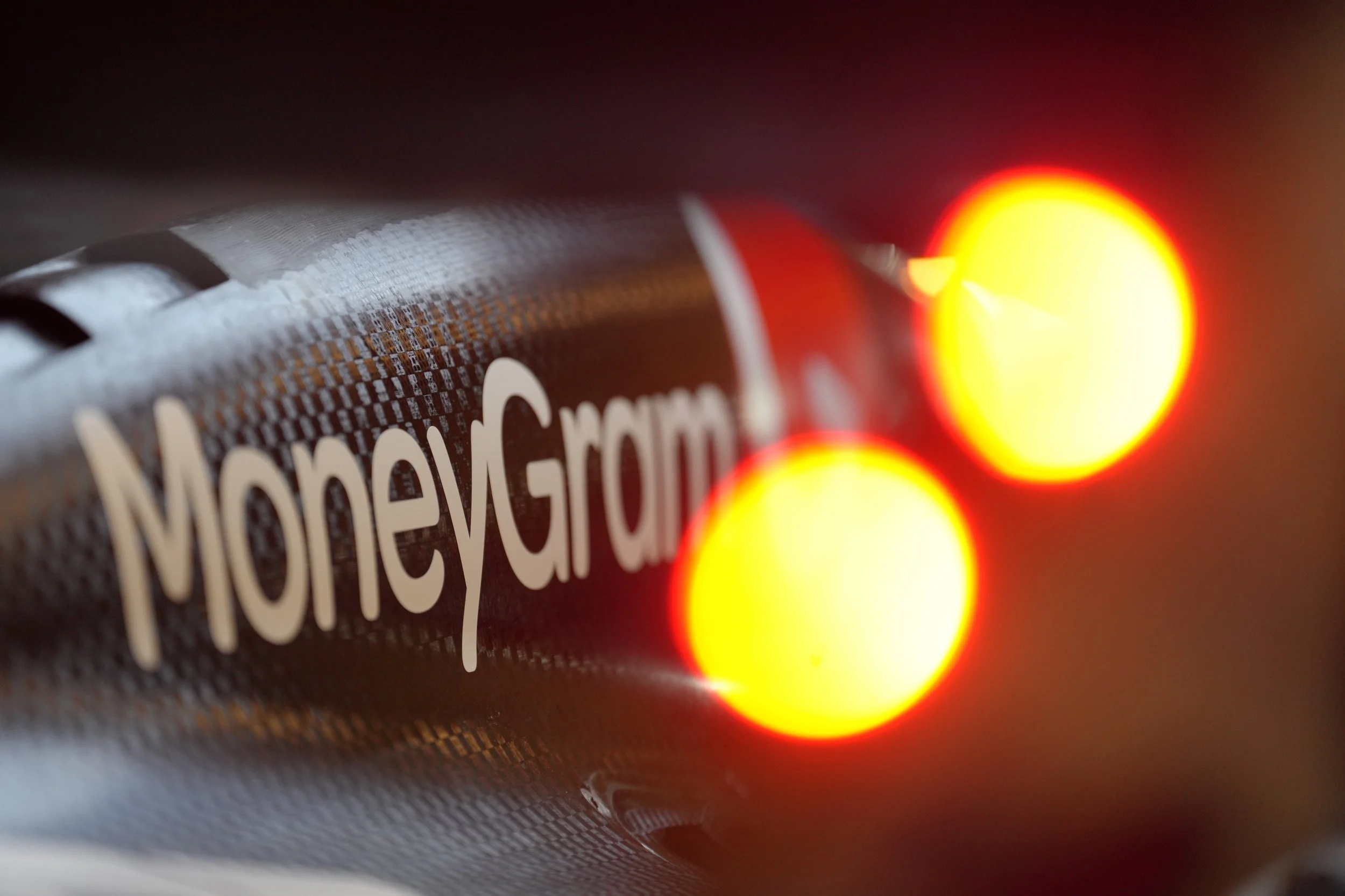 Close-up of a metallic object with the label "MoreyGrom" and two illuminated red and yellow lights in the foreground.