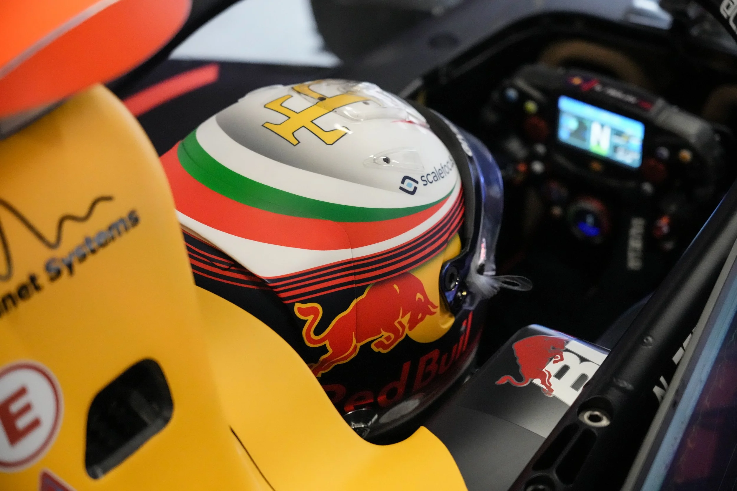 Close-up of a race car driver helmet with Red Bull branding, inside a racing vehicle, alongside a yellow surface that reads 'Smart Streams' and features the Red Bull logo.