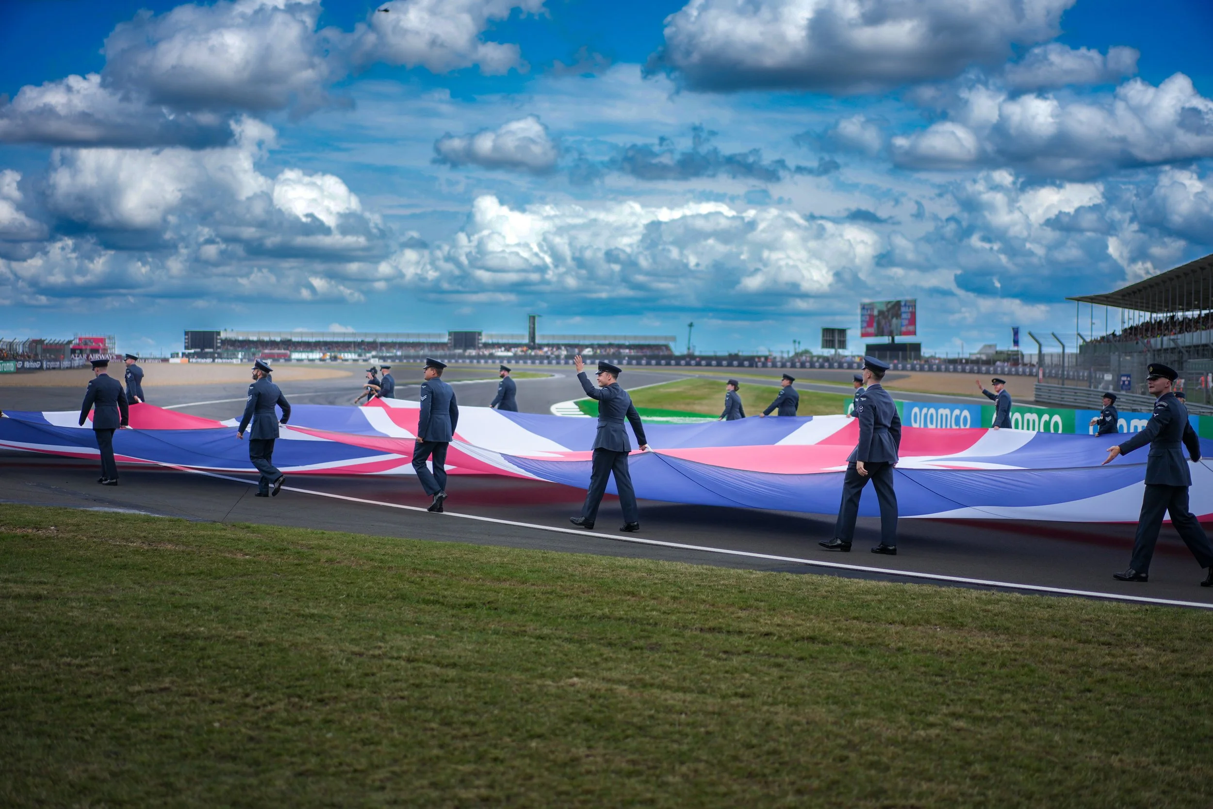 Race track scene with uniformed officials holding a large French flag.