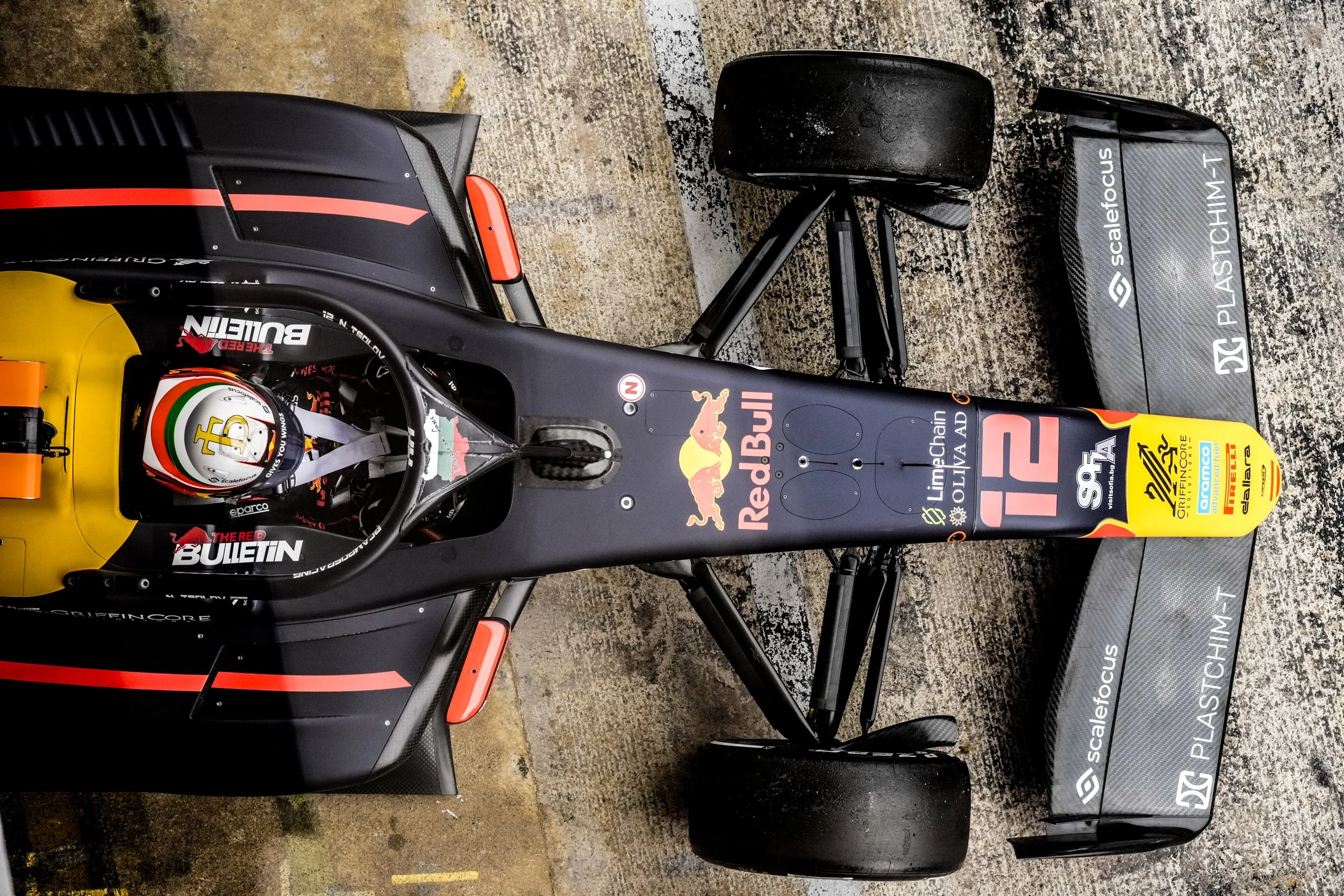 Top-down view of a race car with various sponsor logos, including Red Bull, LimeChain, and ScalarFocus. The car has a black and yellow color scheme, a large rear wing, and a racing driver sitting in the cockpit wearing a helmet.