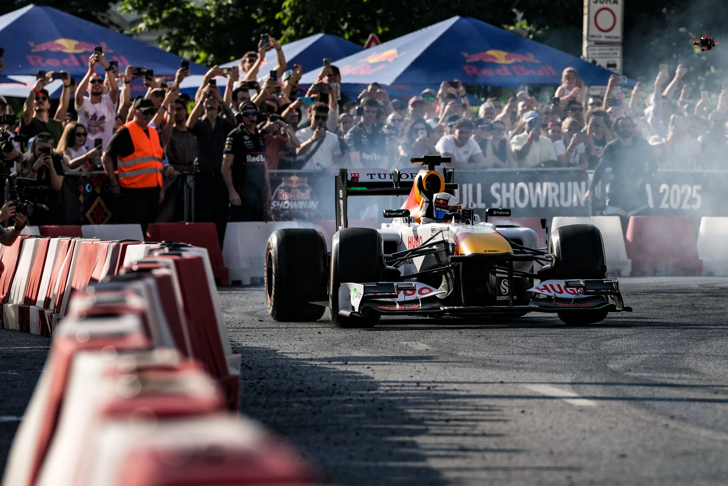 A race car crossing the finish line at a motorsport event with a crowd of spectators watching and taking photos in the background.