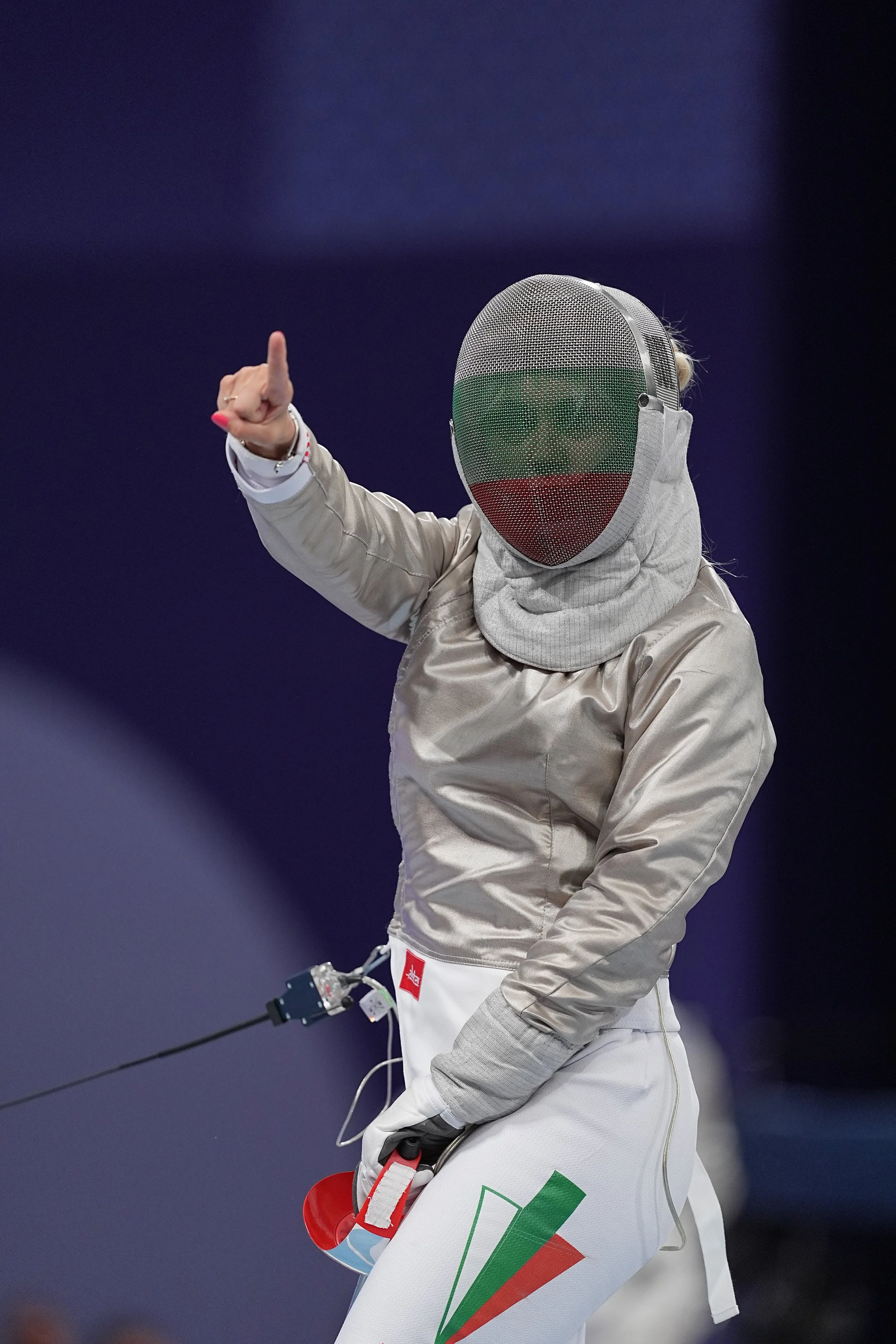 An athlete in fencing gear, including a mask with the Bulgarian flag colors, pointing with one finger and holding a mask in the other hand.