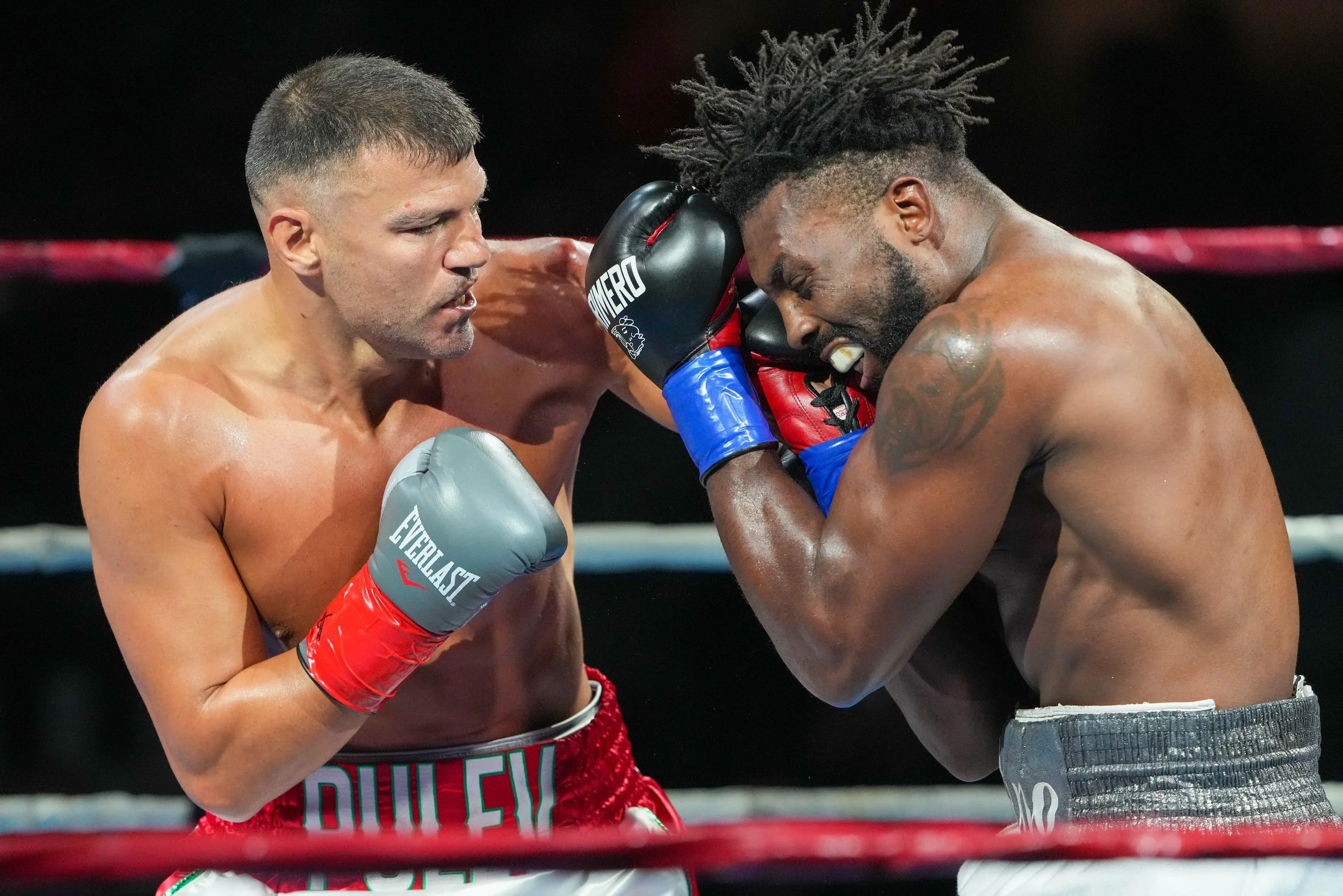 Two male boxers engaged in a match, one throwing a punch and the other defensively blocking, inside a boxing ring.