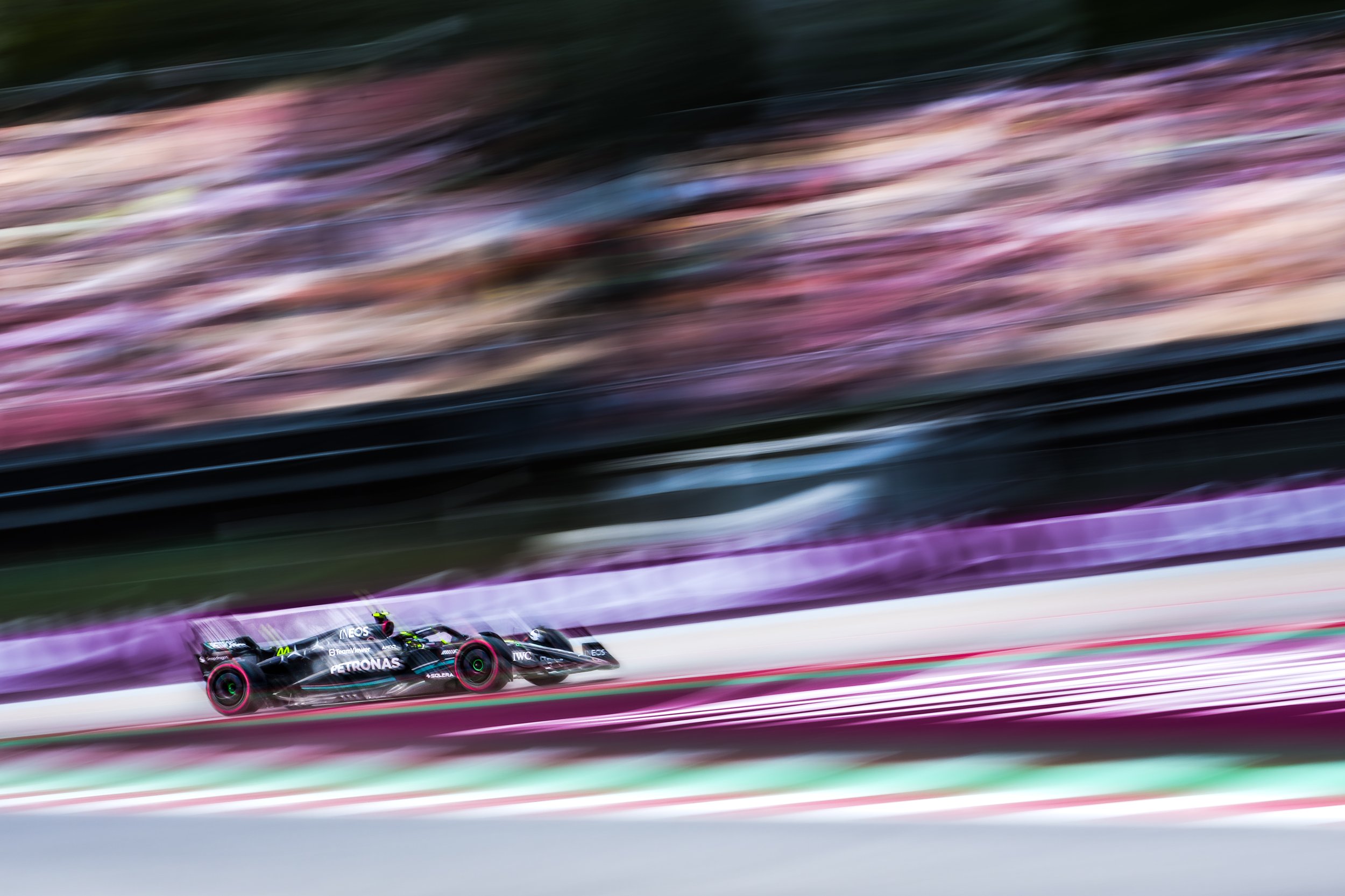 A Formula 1 race car moving at high speed on a race track with colorful blurred background.