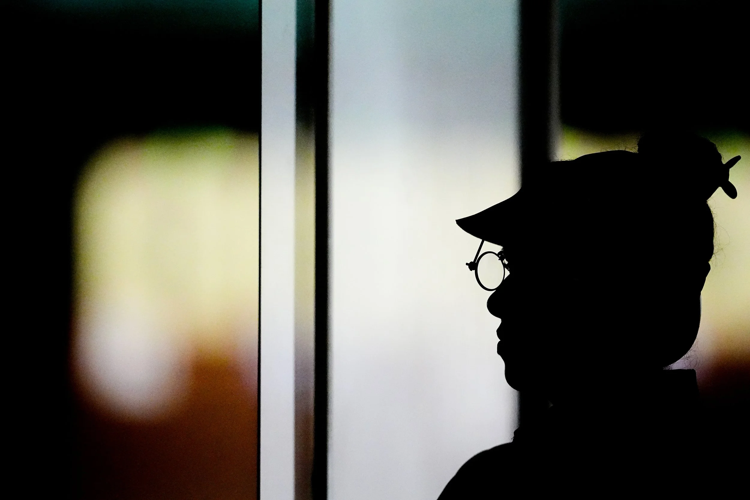 Silhouette of a person wearing glasses and a unicorn hat, looking to the right, with a blurred colorful background.