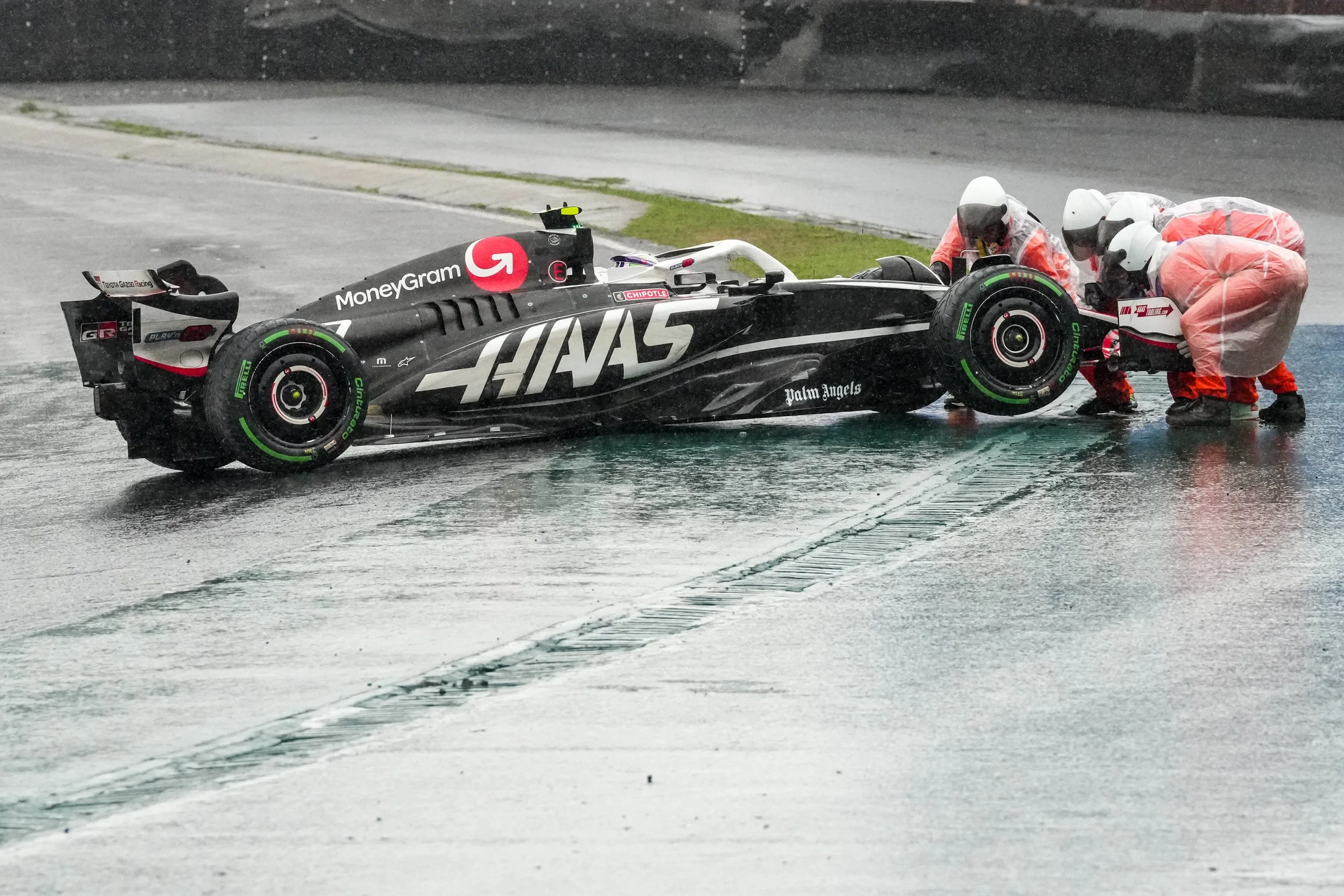 Race car on wet track with four team members in rain gear working on it during rain storm.
