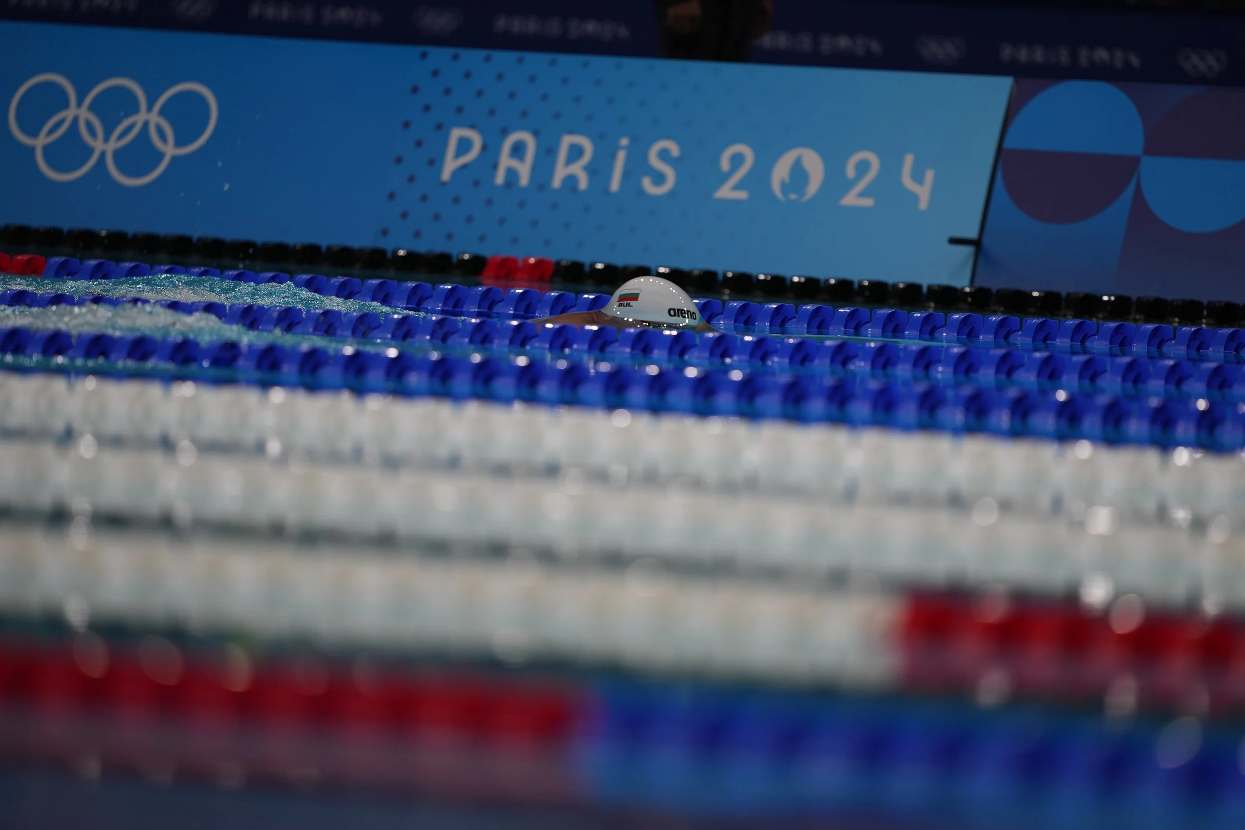 A swimmer in pool celebrating during the Paris 2024 Olympics, with Olympic logo and Paris 2024 sign in the background.