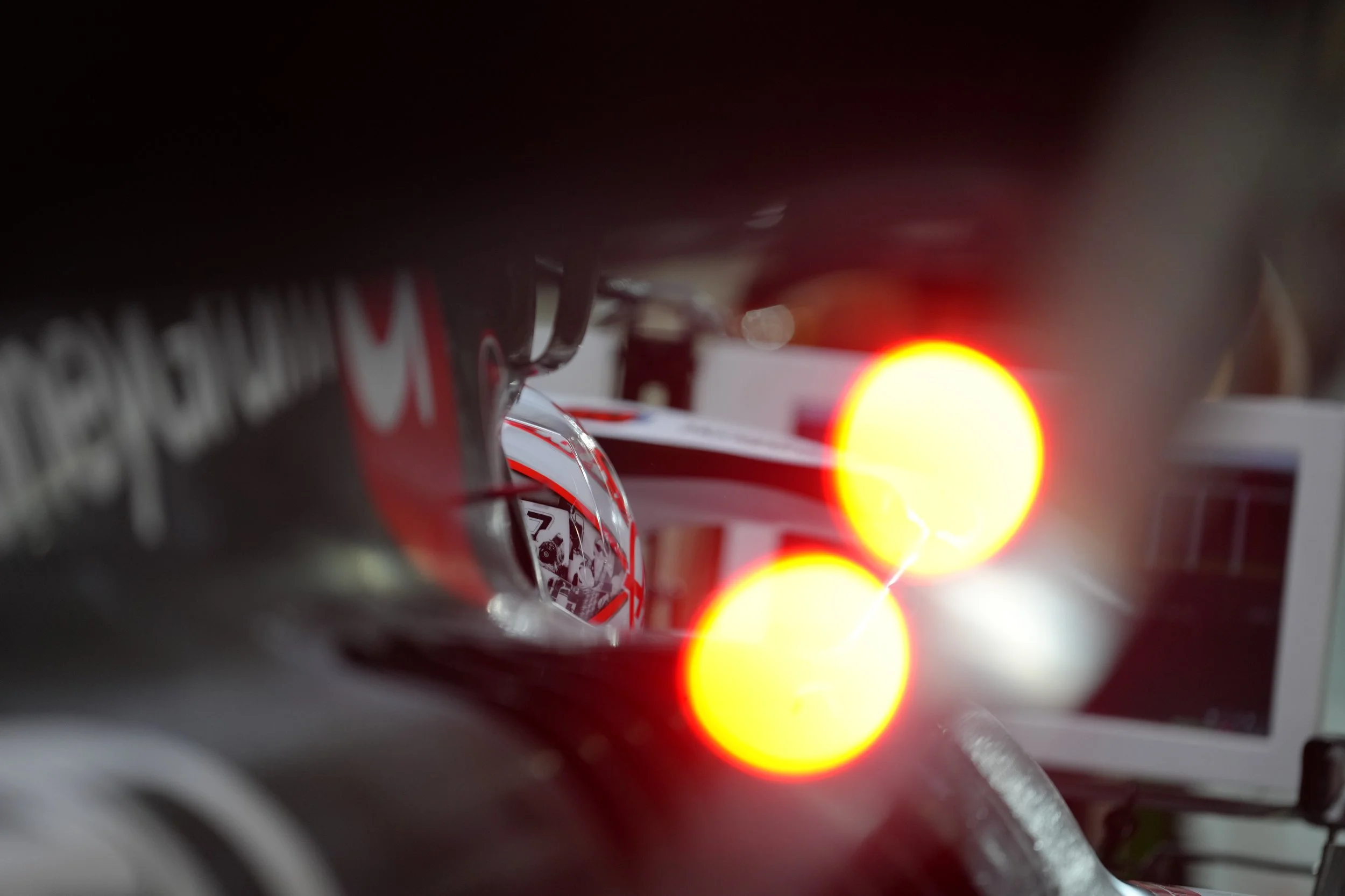 Close-up of a racing car with bright red taillights, with a screen and some equipment in the background.