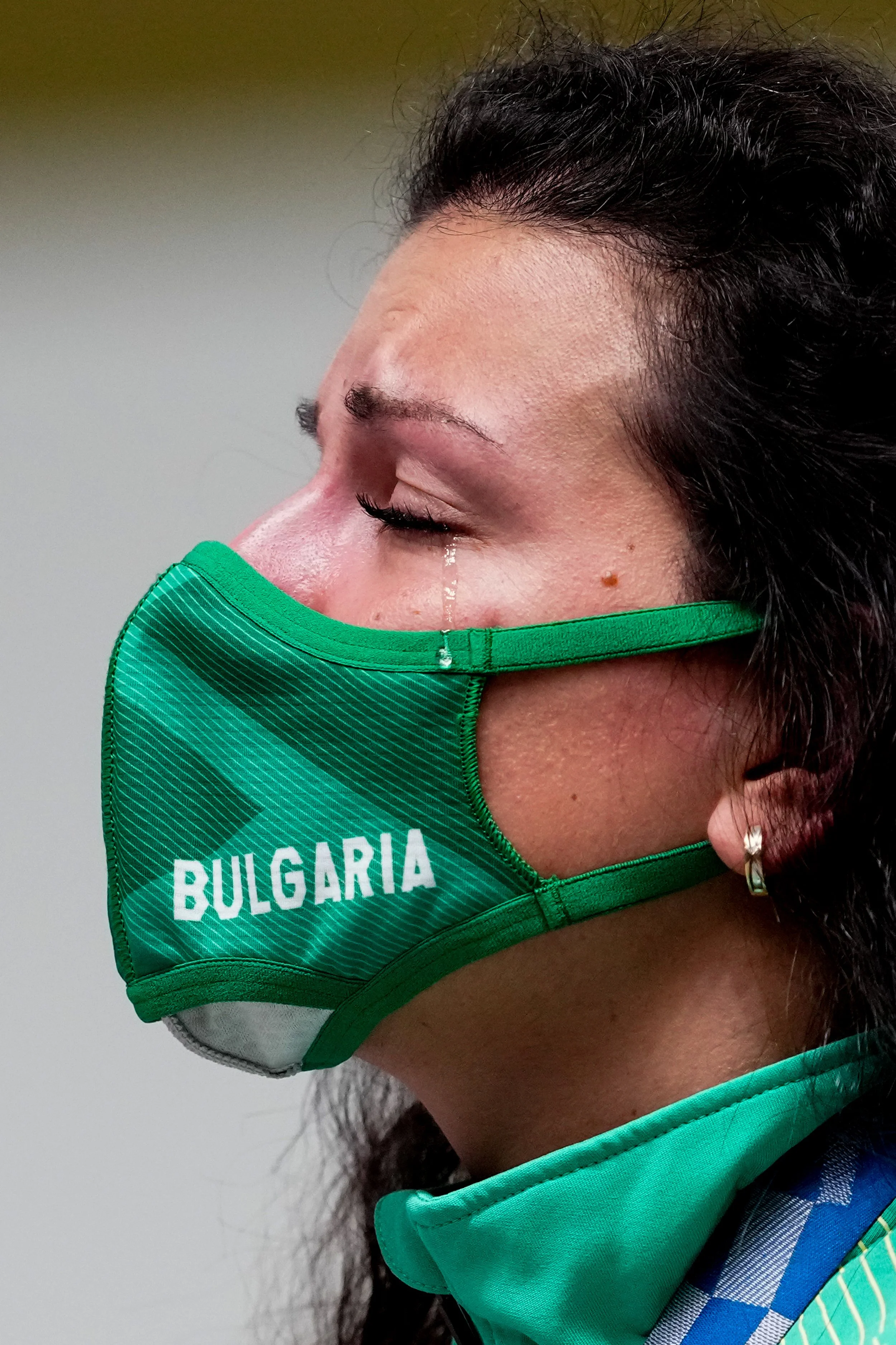 Antoaneta Kostadinova wearing a green face mask with 'BULGARIA' printed on it, tears running from her eyes.