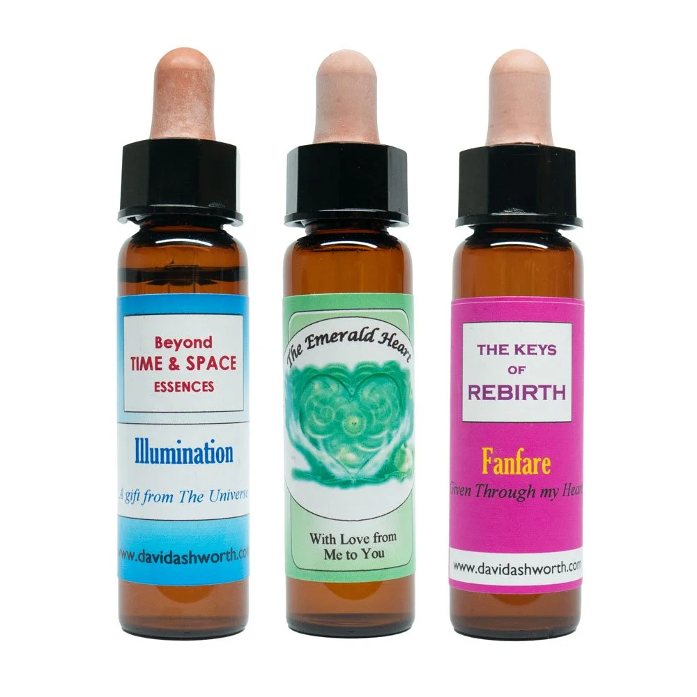 Drei kleine Fläschchen mit Etiketten, die Bezeichnungen wie "Beyond TIME & SPACE ESSENCES," "The Emerald Heart," und "THE KEYS of REBIRTH" anzeigen, jeweils mit einer Pipette auf der Oberseite.