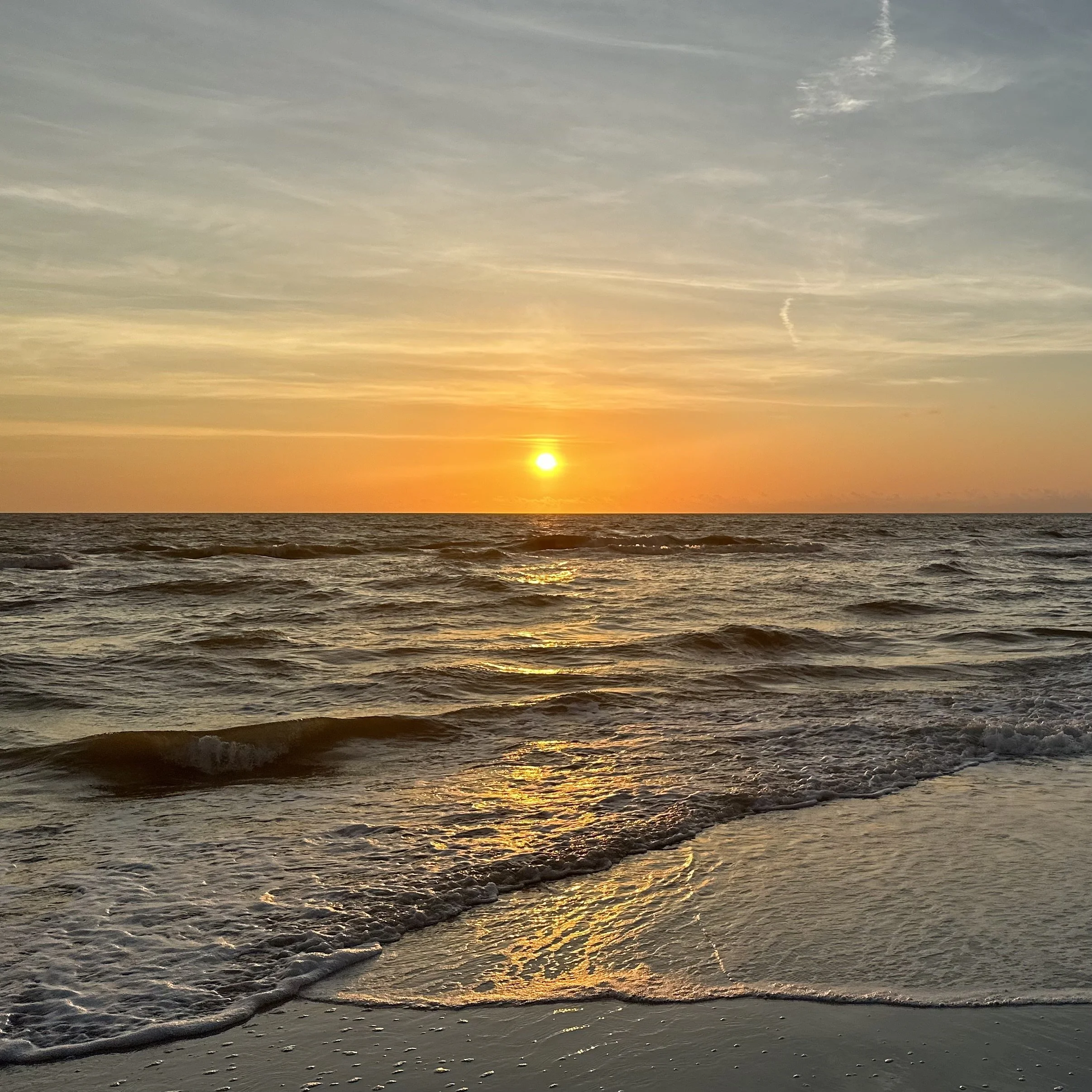 Sonnenuntergang über dem Meer mit Wolken am Himmel und Wellen am Strand.