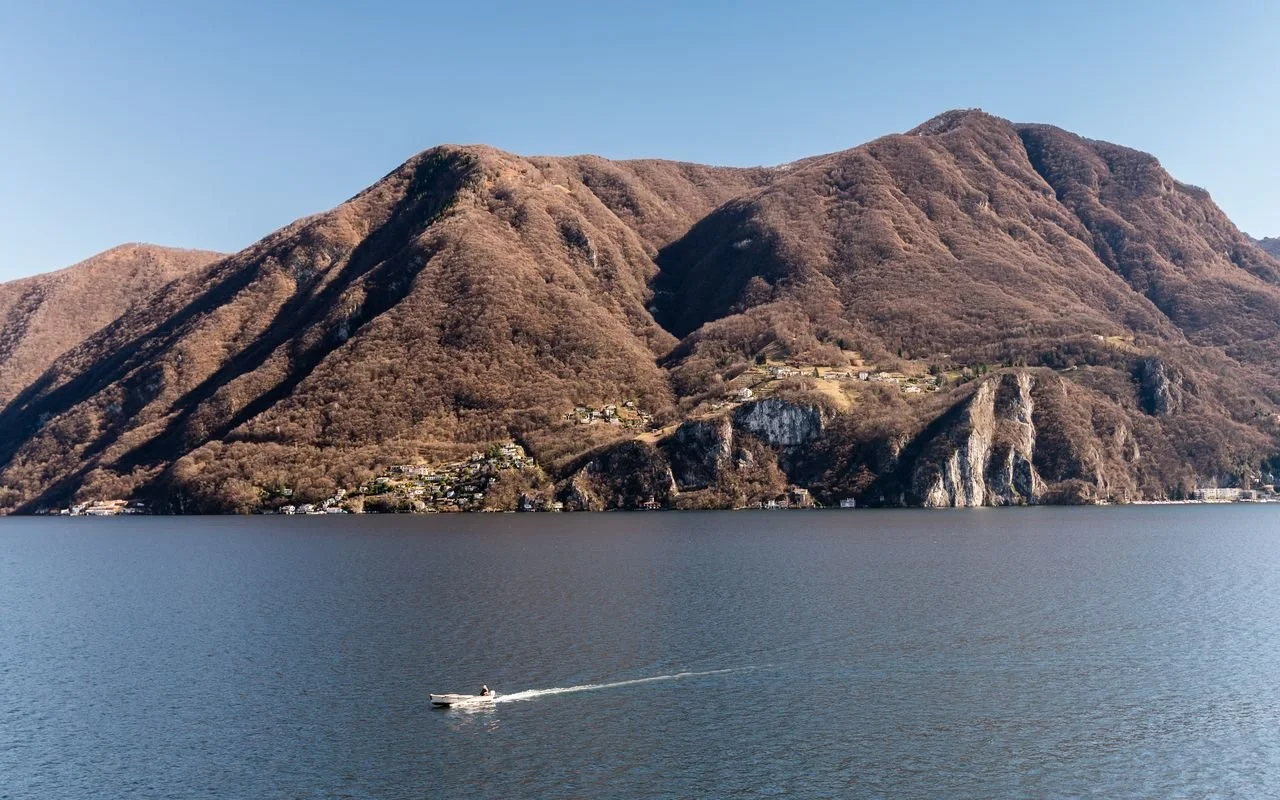 Vista di un lago con montagne in background e una barca che naviga sull'acqua.