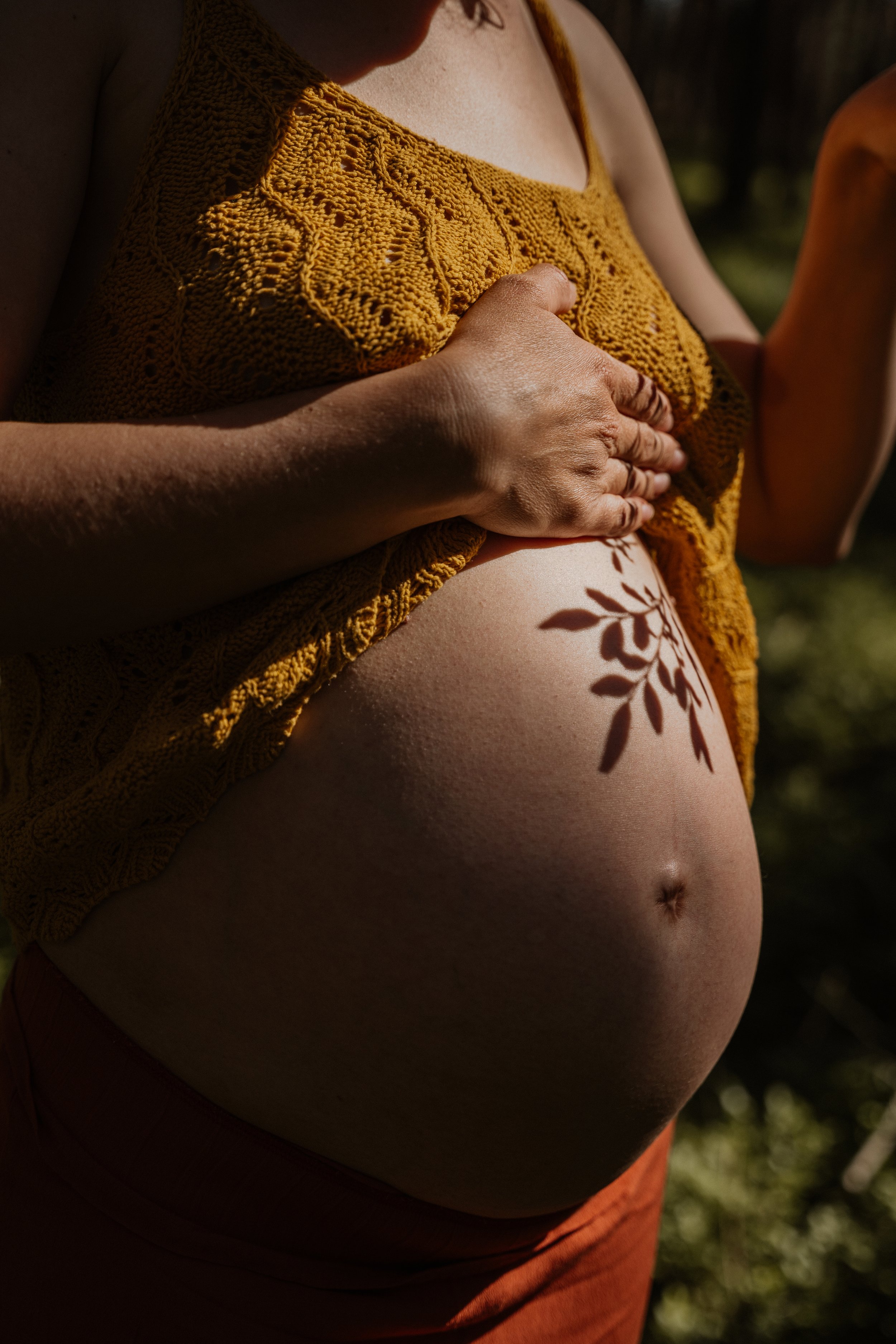 Ast wirft Schatten auf wachsenden Babybauch. Ausdruck von Wärme, Verbundenheit und Vorfreude auf die Geburt. Doula-Begleitung in Bayreuth.