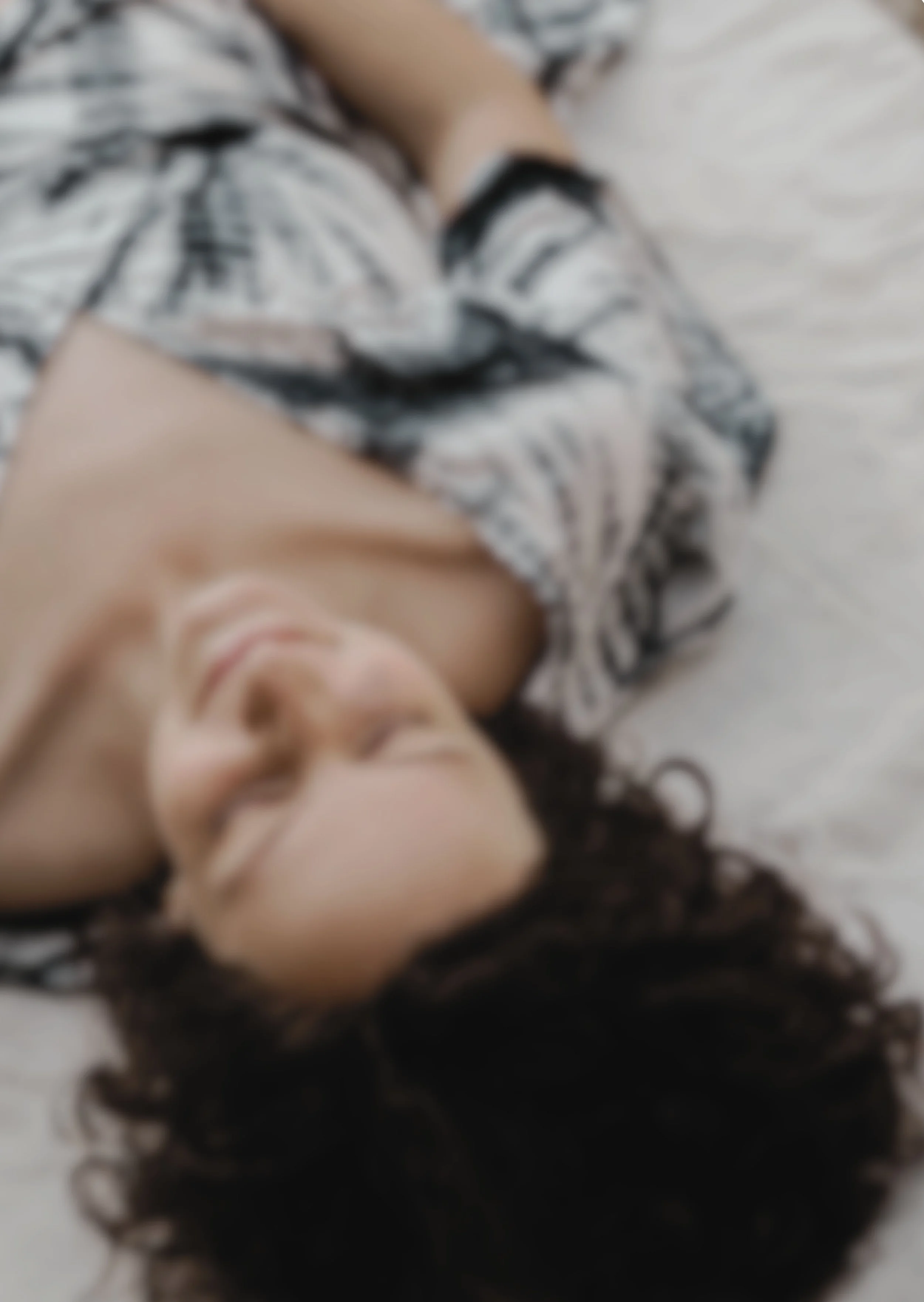 Blurry Aufnahme einer Frau, die auf einer weißen Decke liegt, mit geschlossenen Augen und einem entspannen Gesichtsausdruck.