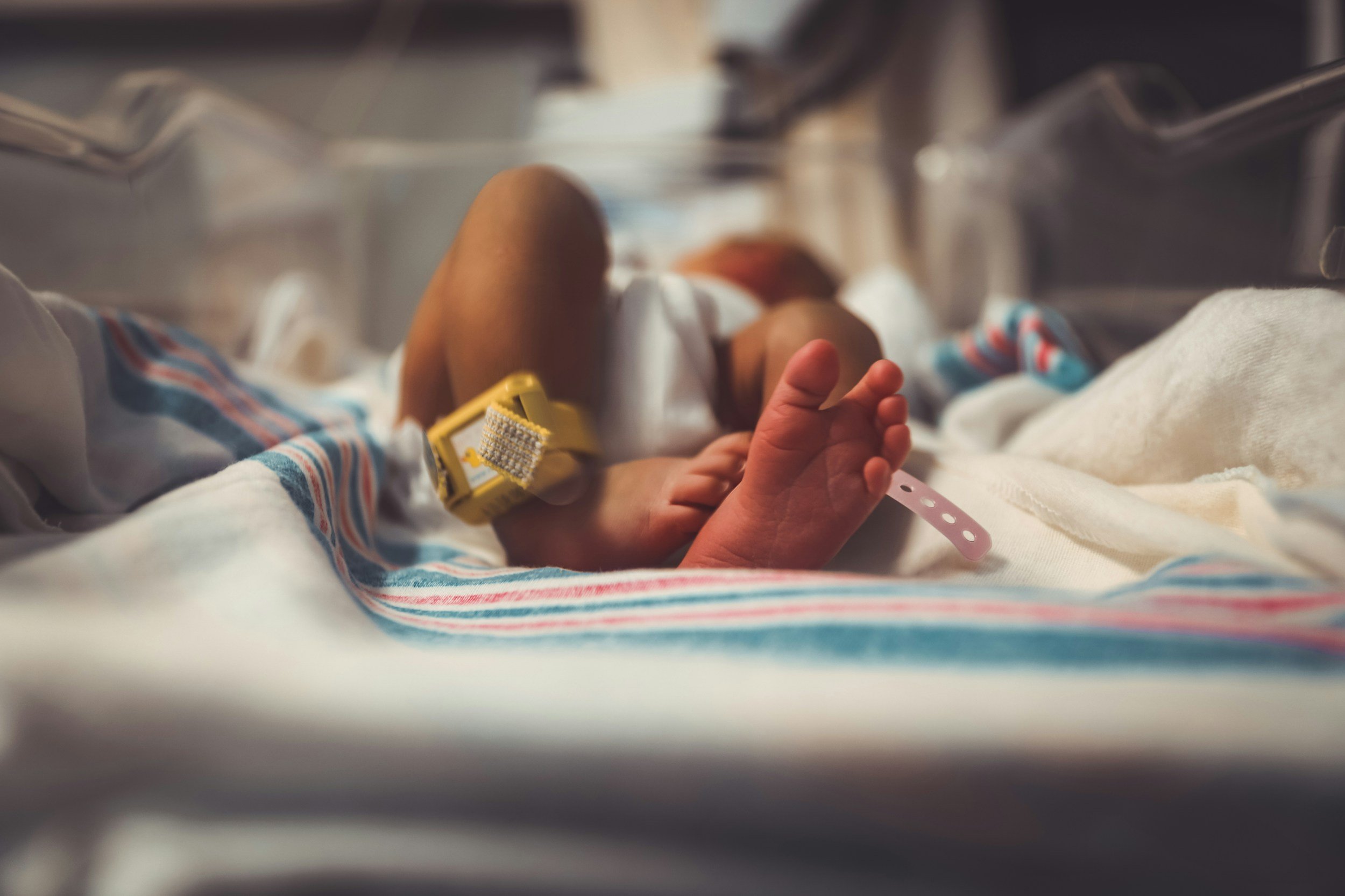 Newborn baby lying in hospital bassinet, viewed from the feet, with standard Ontario hospital blanket and ankle ID tags visible, representing postpartum care and support.
